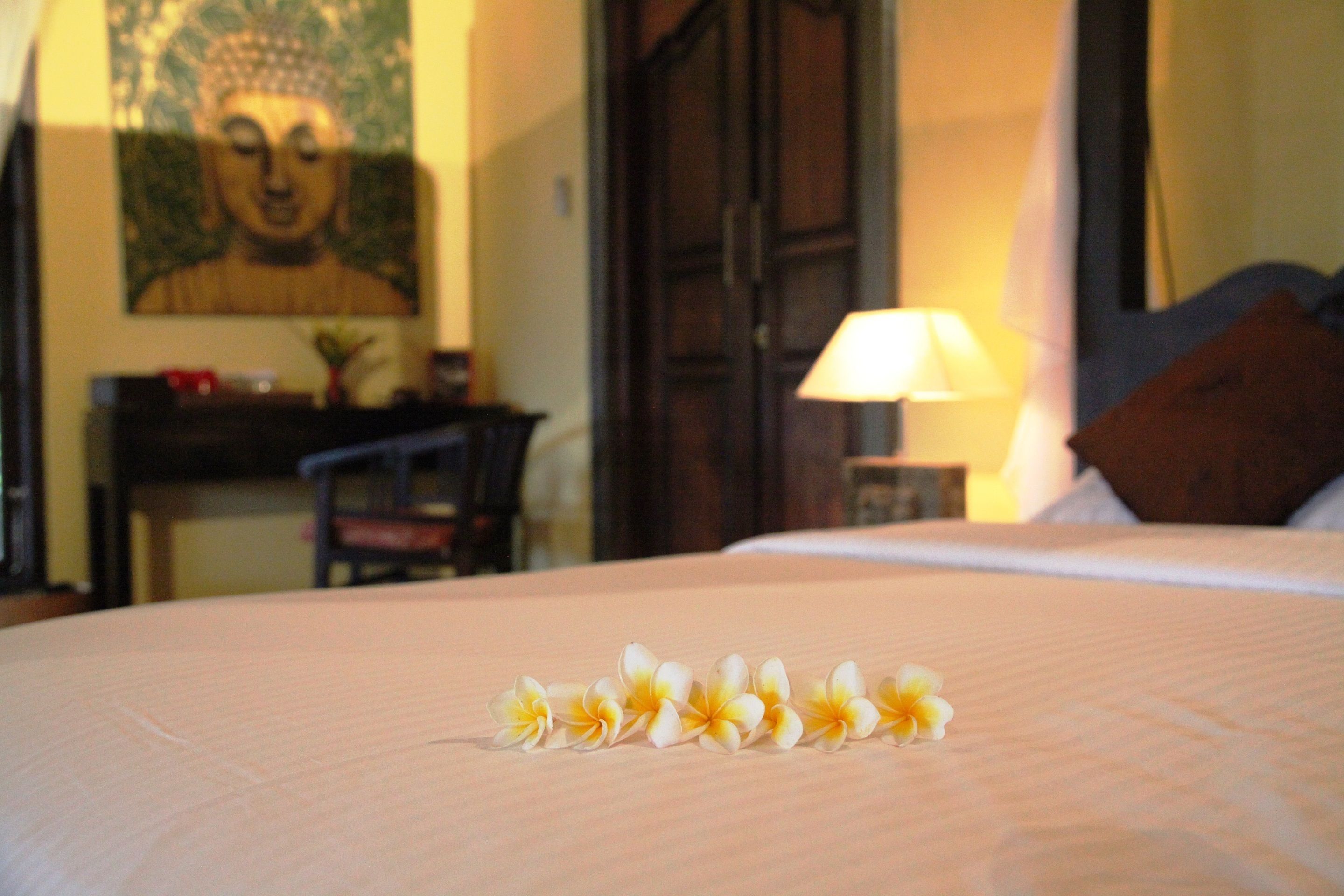 Una cama con un arreglo floral, un cuadro de Buda y una lámpara en una habitación de hotel.