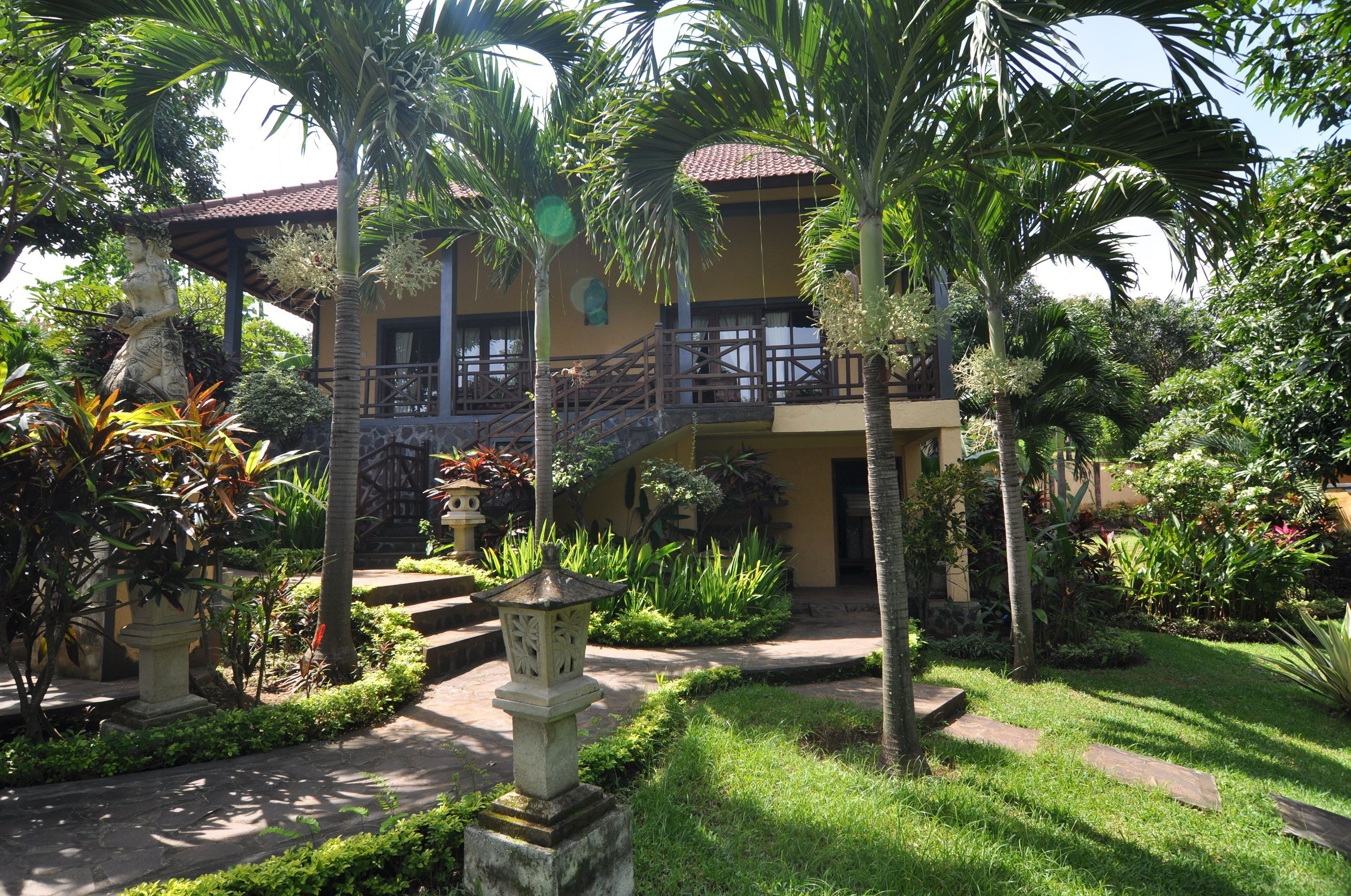 A two-story building with a balcony, surrounded by lush greenery and palm trees.