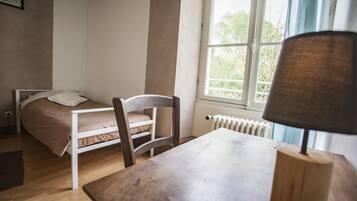 Une chambre à coucher avec un lit, une chaise, une table et une fenêtre donnant sur des arbres.