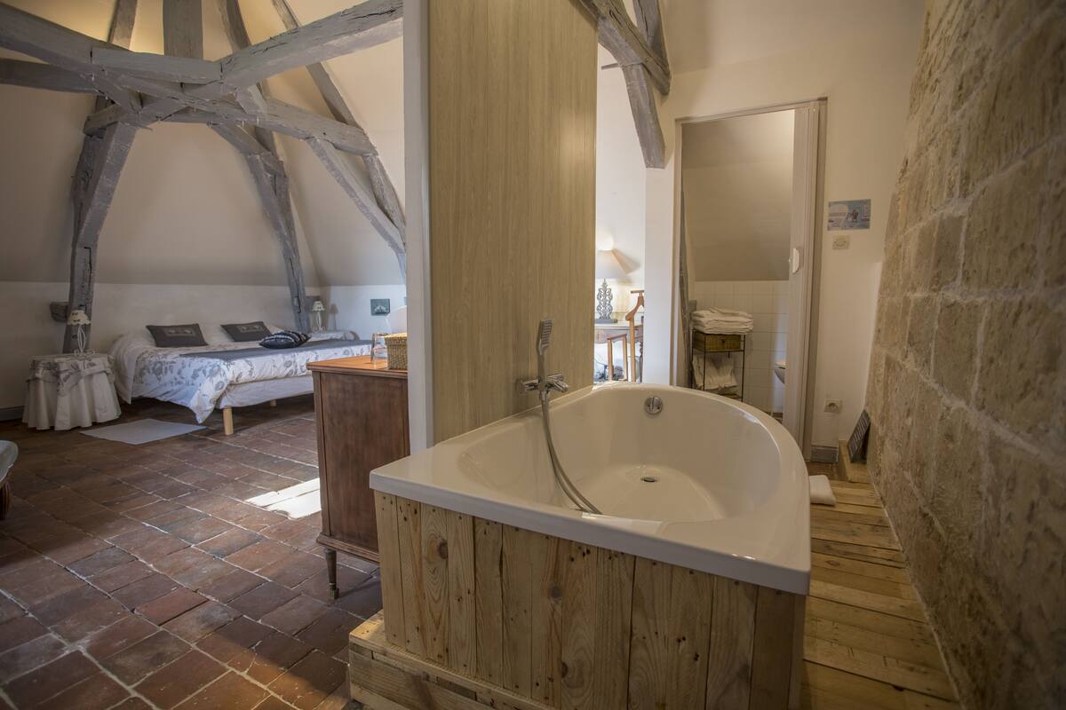 Een rustieke slaapkamer met zichtbare houten balken, een houten badkuip en een tegelvloer.