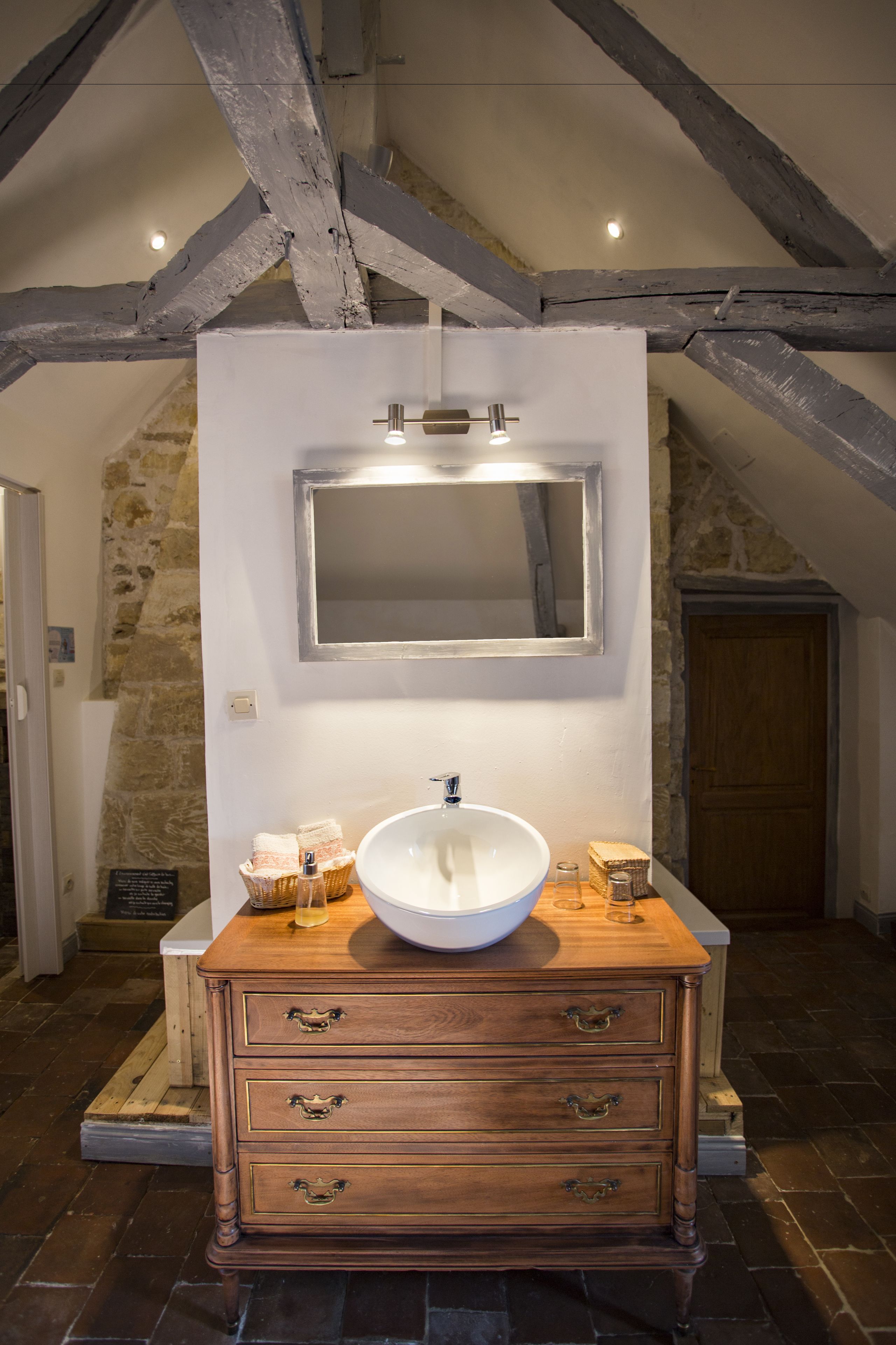 A bathroom with a white sink, wooden vanity, and a stone wall.