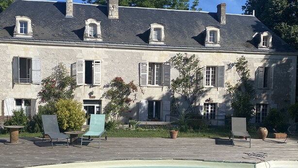 Una zona de piscina con sillas de descanso y un edificio de piedra con ventanas y contraventanas.