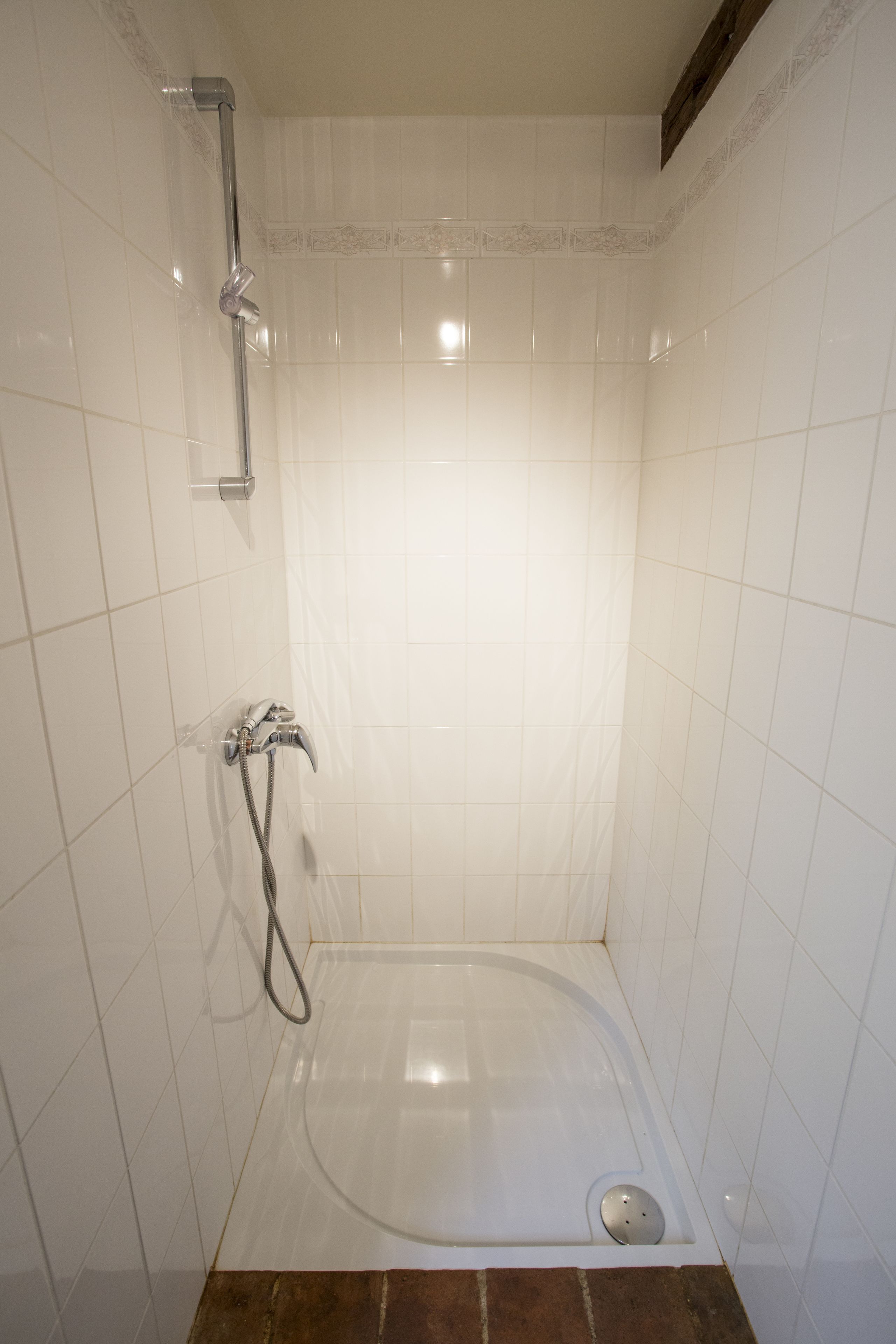 Un baño pequeño con azulejos blancos, una bañera, un cabezal de ducha manual y un grifo empotrado.