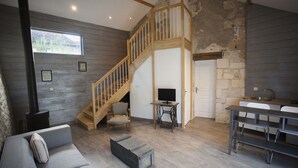 Un área de estar tipo loft con una escalera de madera, un sofá, una televisión y una zona de cocina.