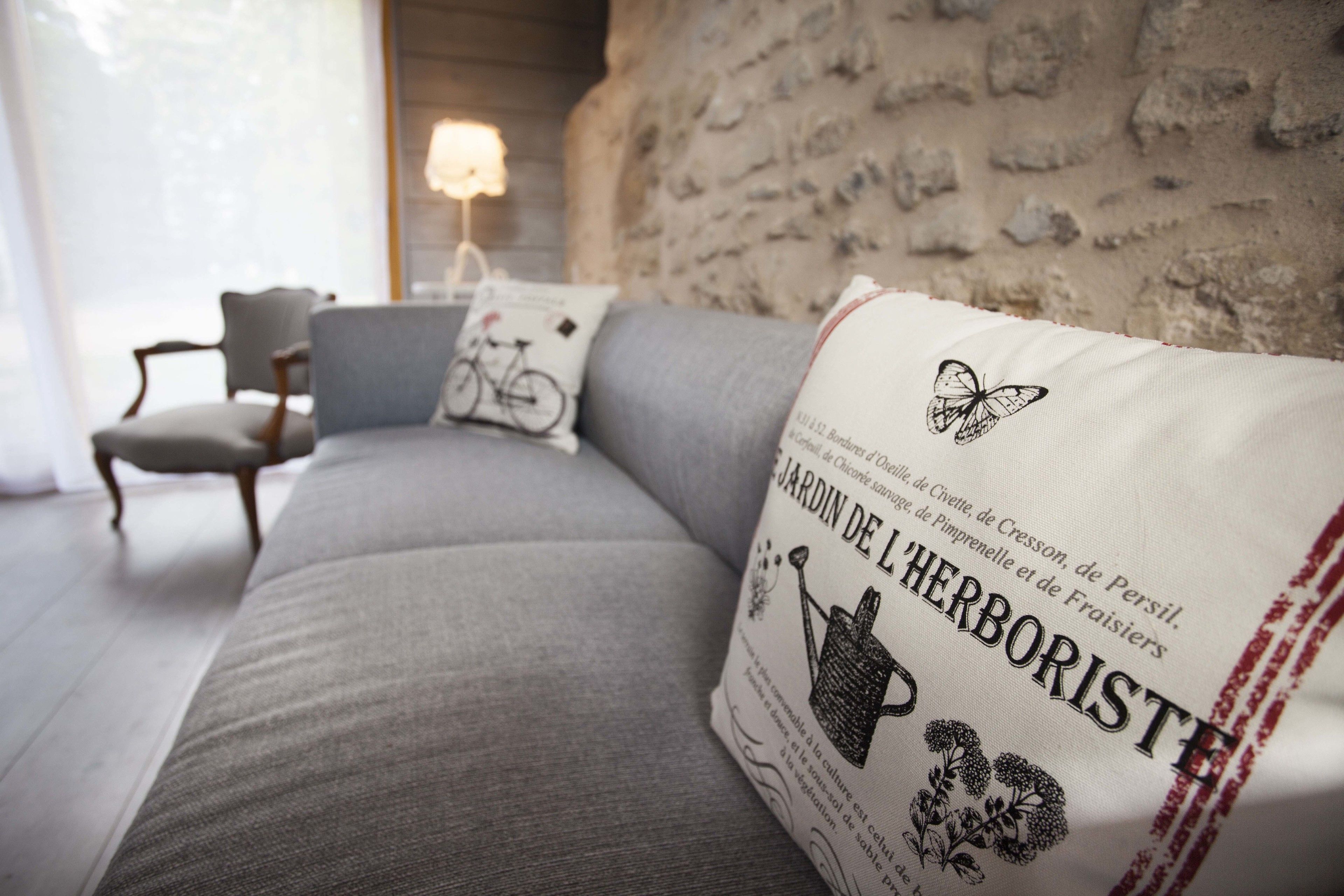 Een moderne woonkamer met een grijze bank, een decoratief kussen en een lamp op de achtergrond.