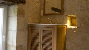 Un baño rústico con pared de piedra, armarios de madera y un espejo.