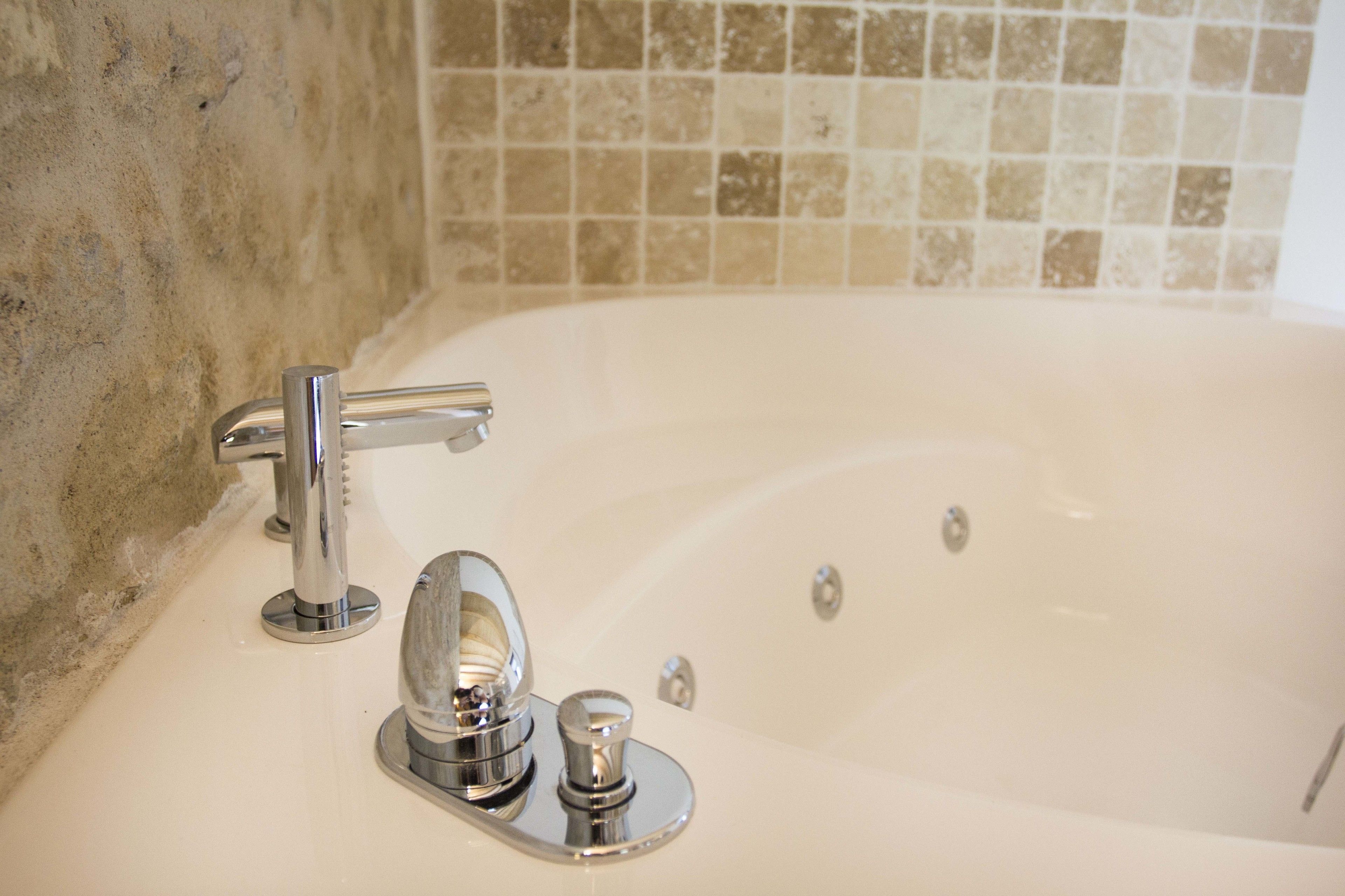 Une salle de bain avec une baignoire, un robinet chromé et un mur carrelé.