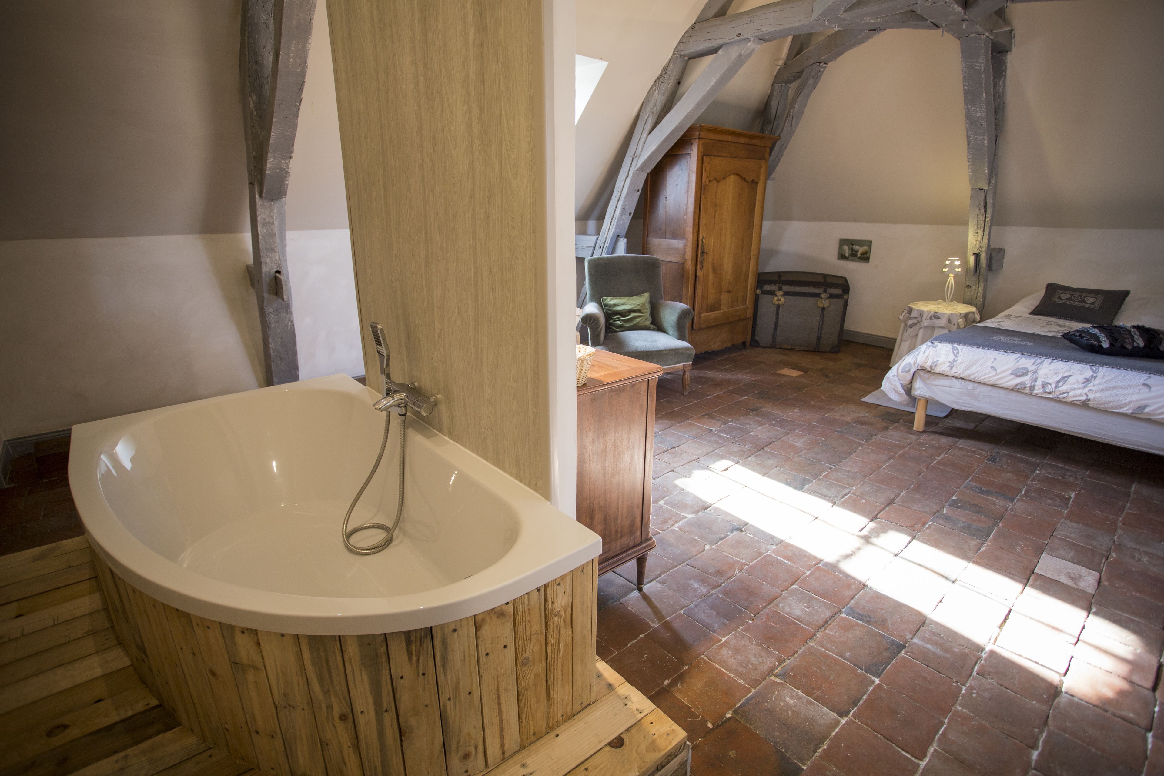 Un dormitorio con una bañera grande, vigas de madera, una cama y una pequeña mesa.
