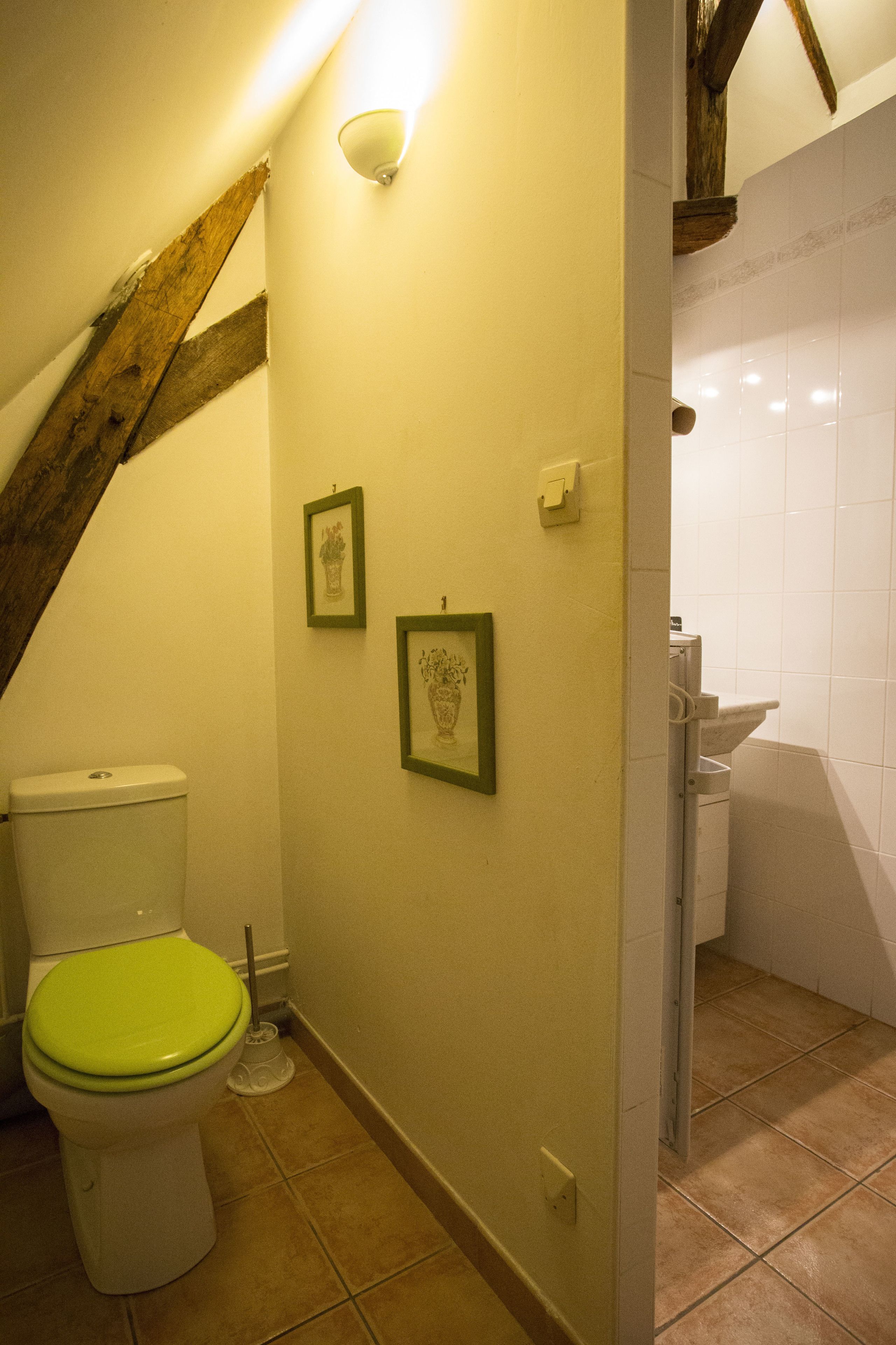 A bathroom with a toilet, framed pictures on the wall, and a shower area.