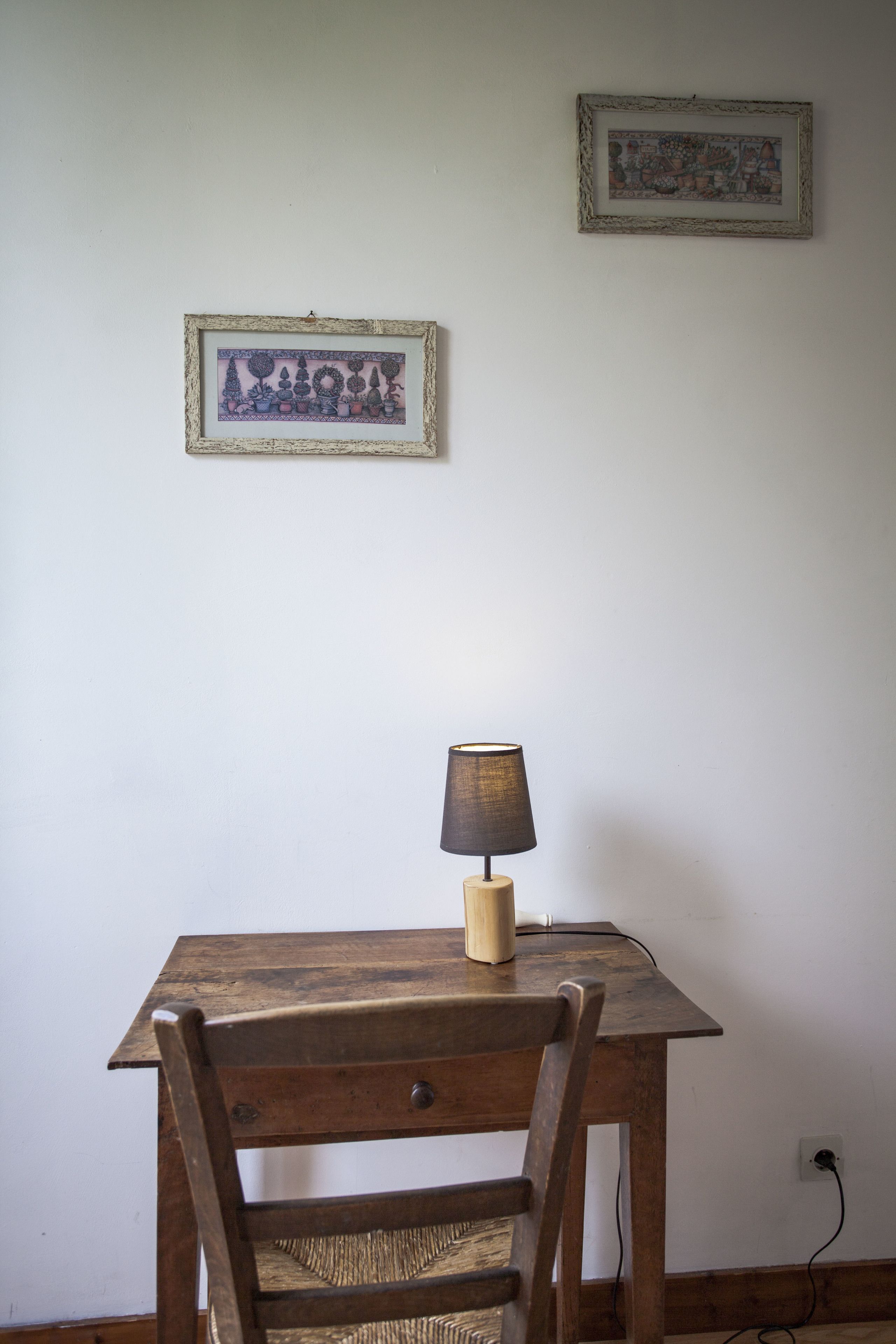 A wooden table with a lamp and a chair in front of it. There are two framed pictures on the wall above.