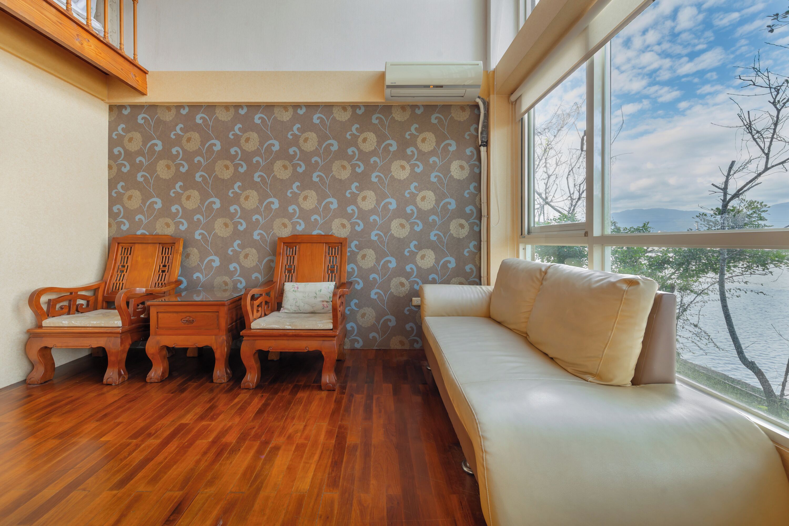 Une pièce avec un plancher en bois, un canapé, deux chaises en bois, une petite table et un papier peint à motifs.