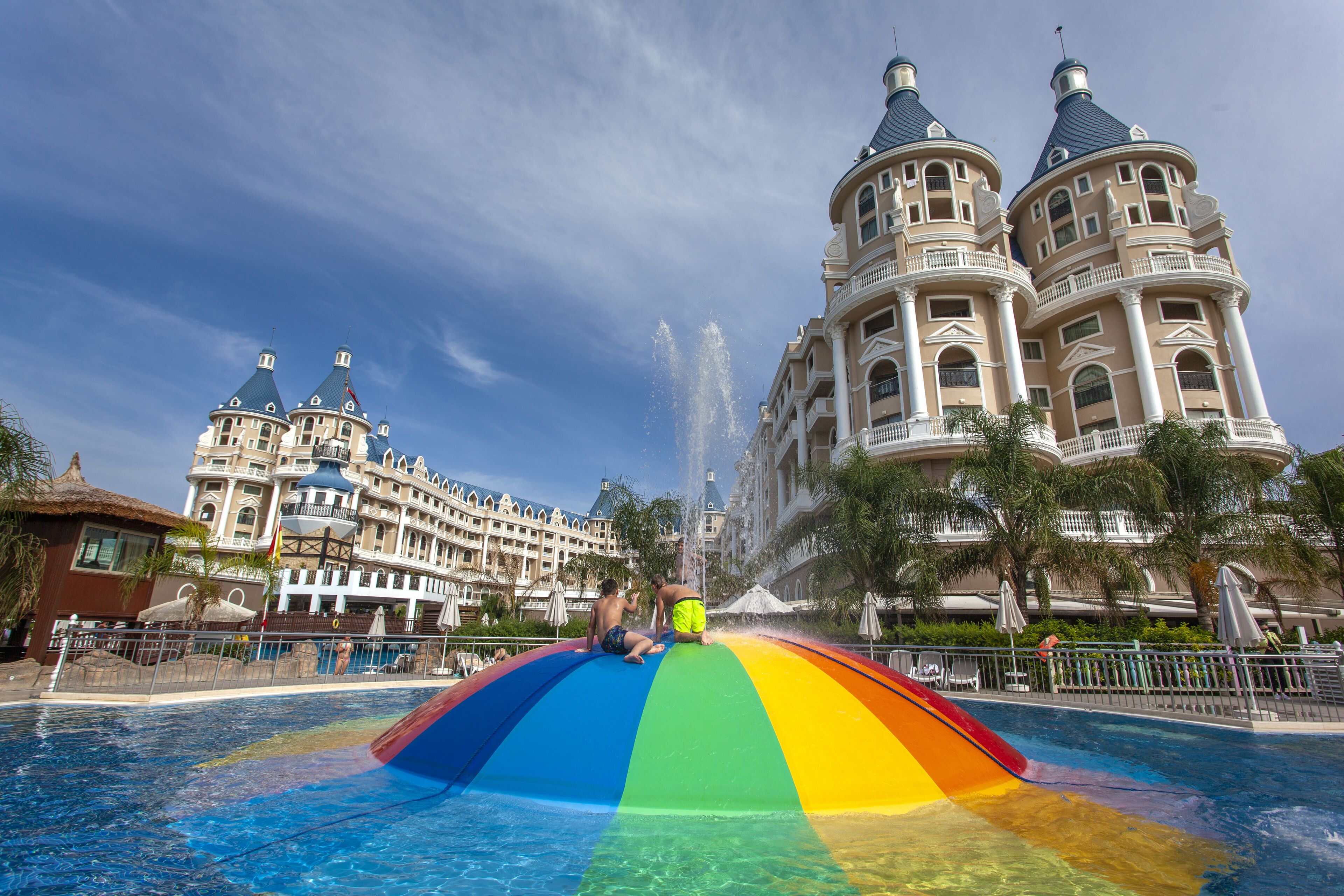 Un tobogán acuático grande con diseño de arcoíris, una piscina y un hotel imponente con múltiples torres al fondo.