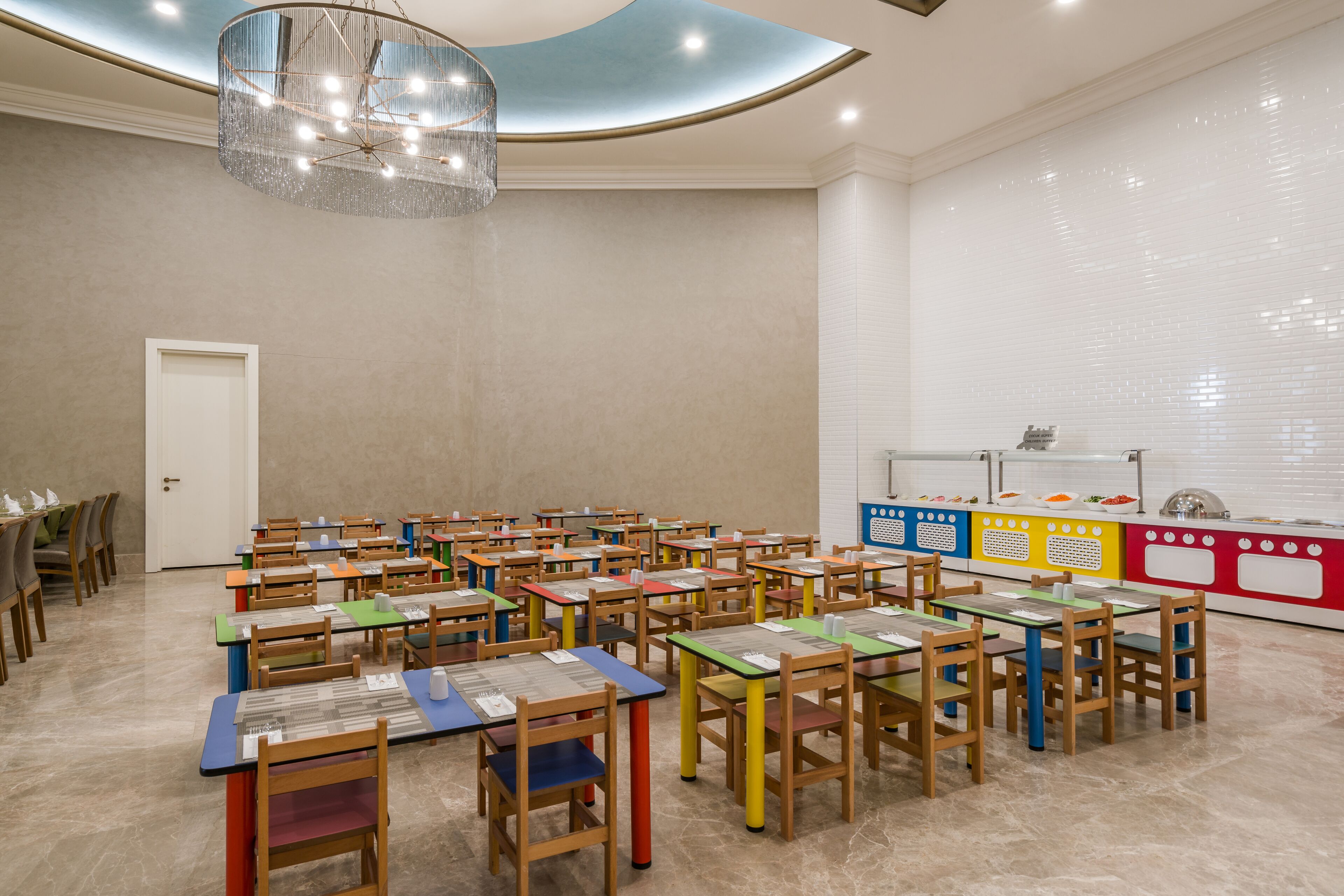 Un salón de conferencias con varias mesas y sillas, una araña y una zona de buffet con exhibiciones de comida.