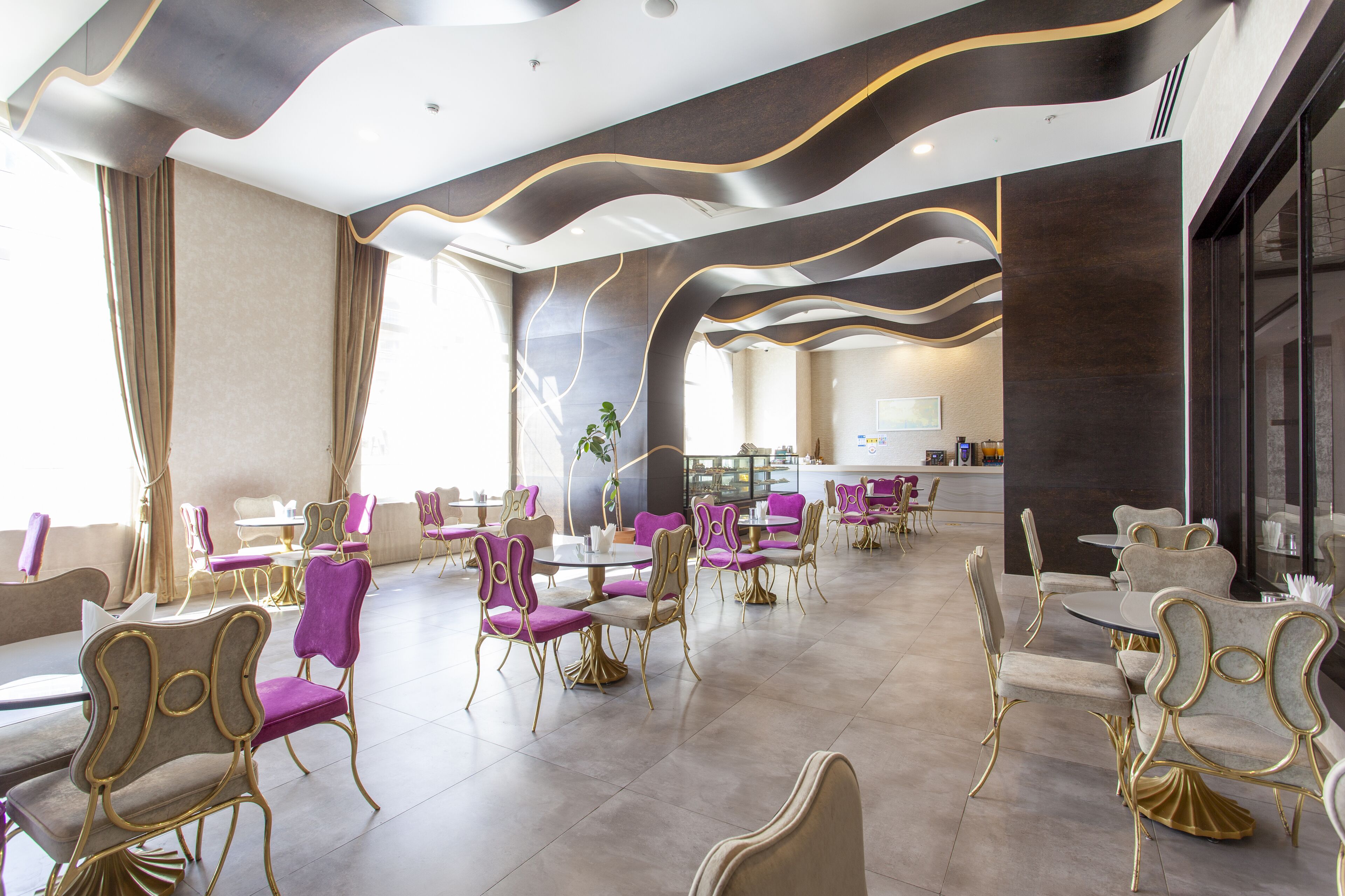 Un'area ristorazione moderna con sedie viola e dorate, un bancone centrale e vista sulla città.