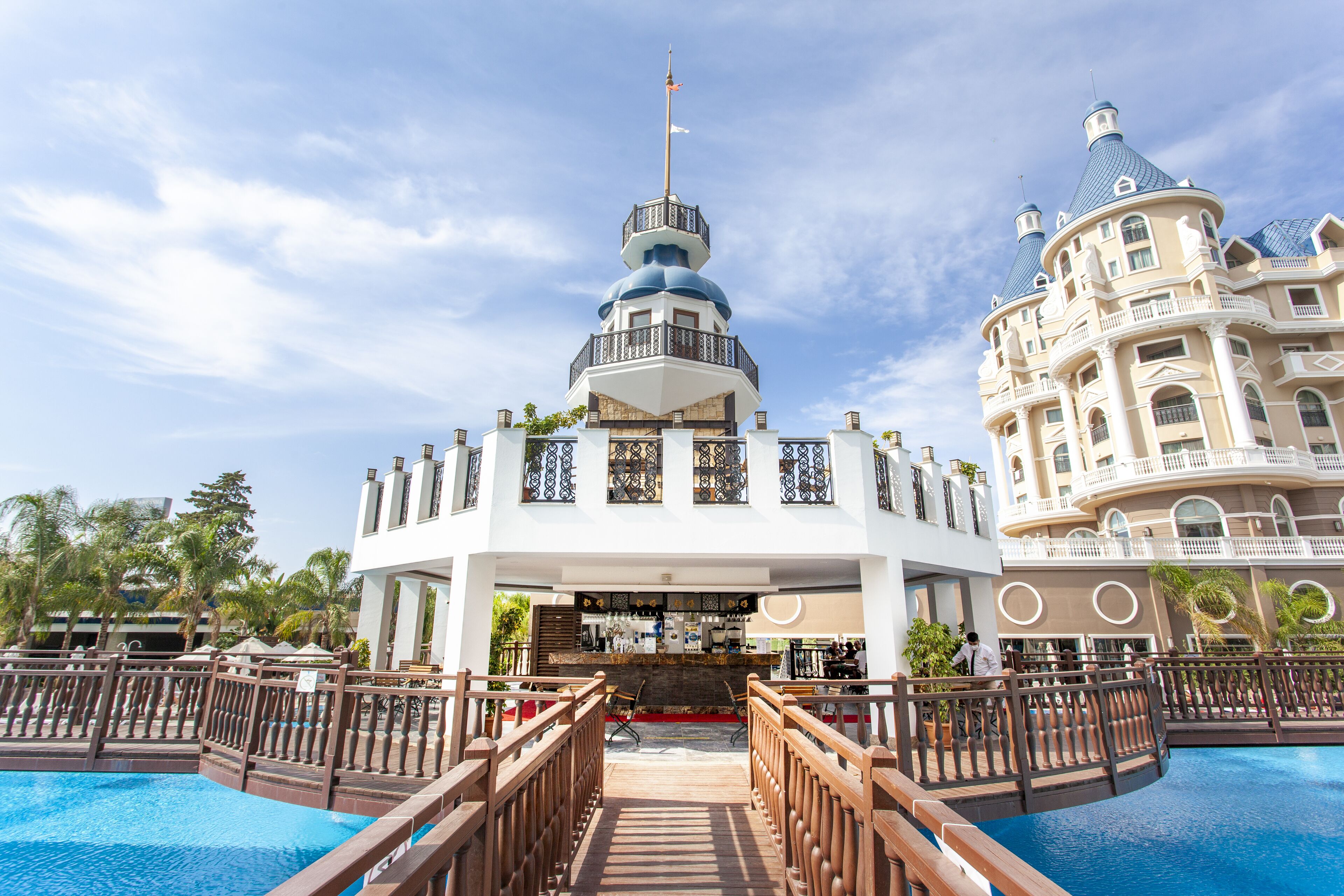 Un resort con un bar central, piscina y un edificio grande con múltiples balcones.
