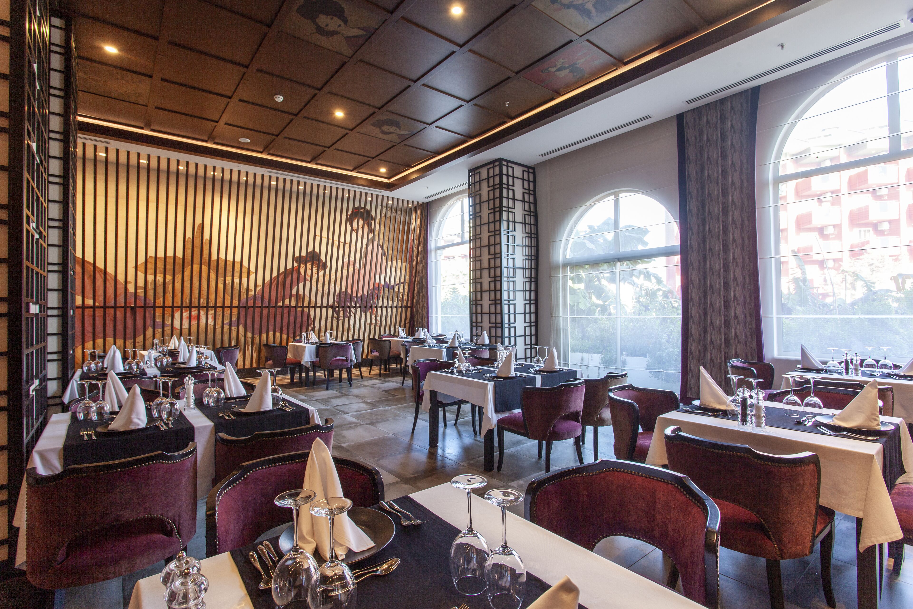 Un restaurante con mesas dispuestas para comer, que presenta una decoración moderna con una combinación de sillas rojas y negras, y ventanas grandes que aportan luz natural.