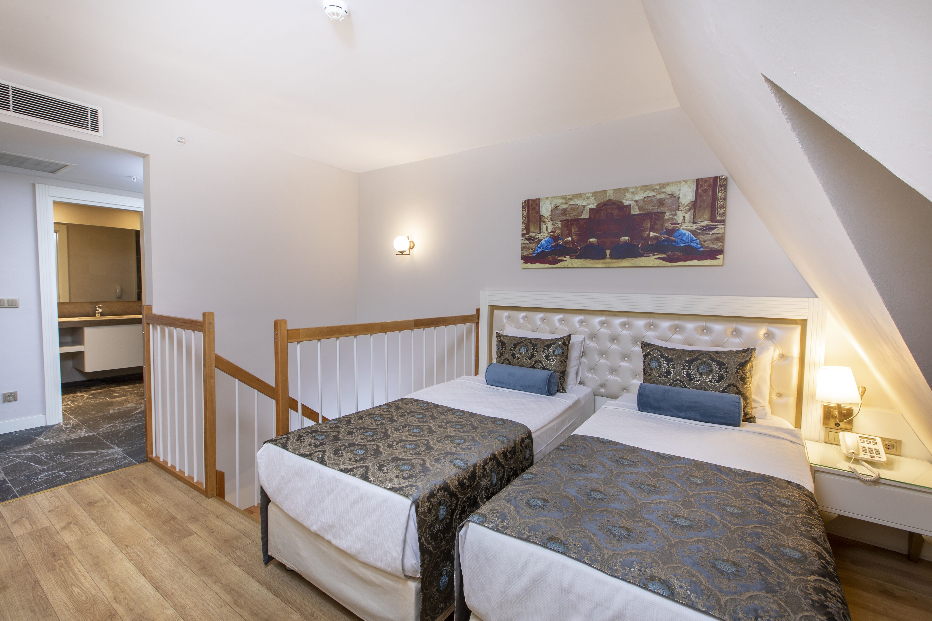 A bedroom with two beds, a painting on the wall, and a nightstand with a lamp.