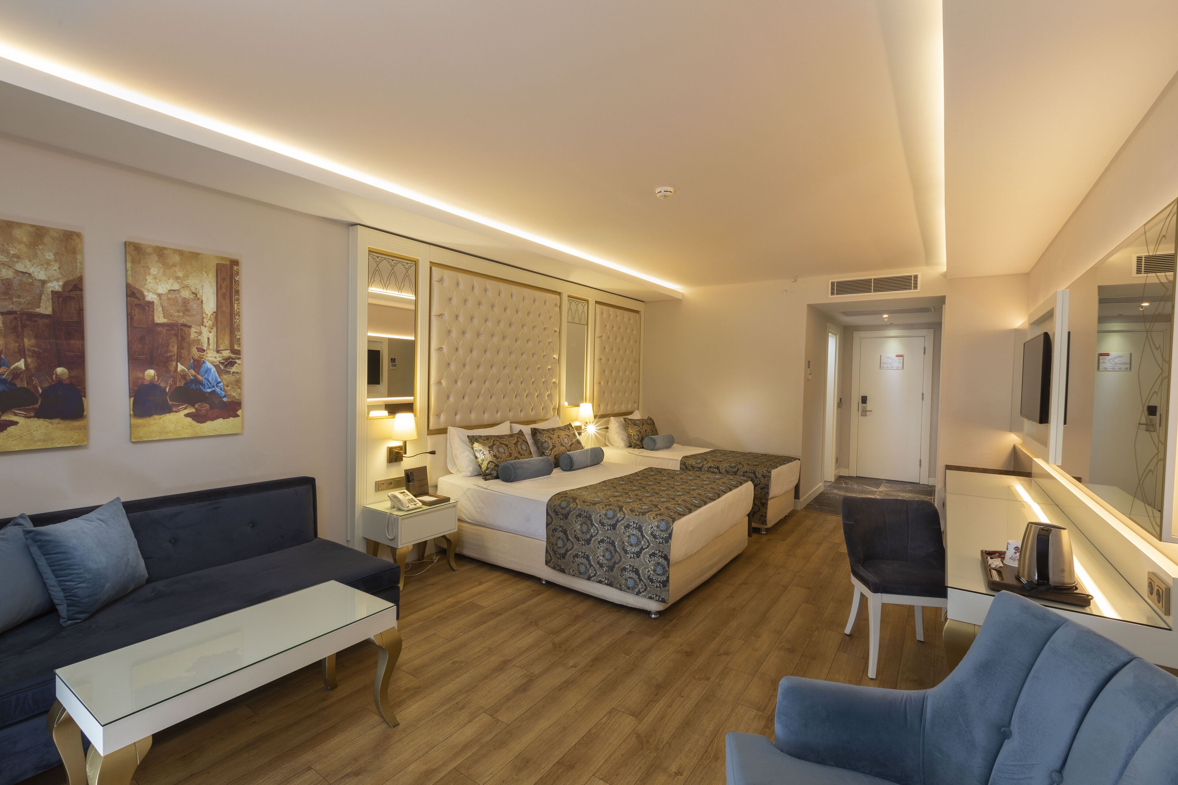 Una habitación de hotel con una cama grande, un sofá, una silla y un escritorio. Hay cuadros en la pared y un televisor.