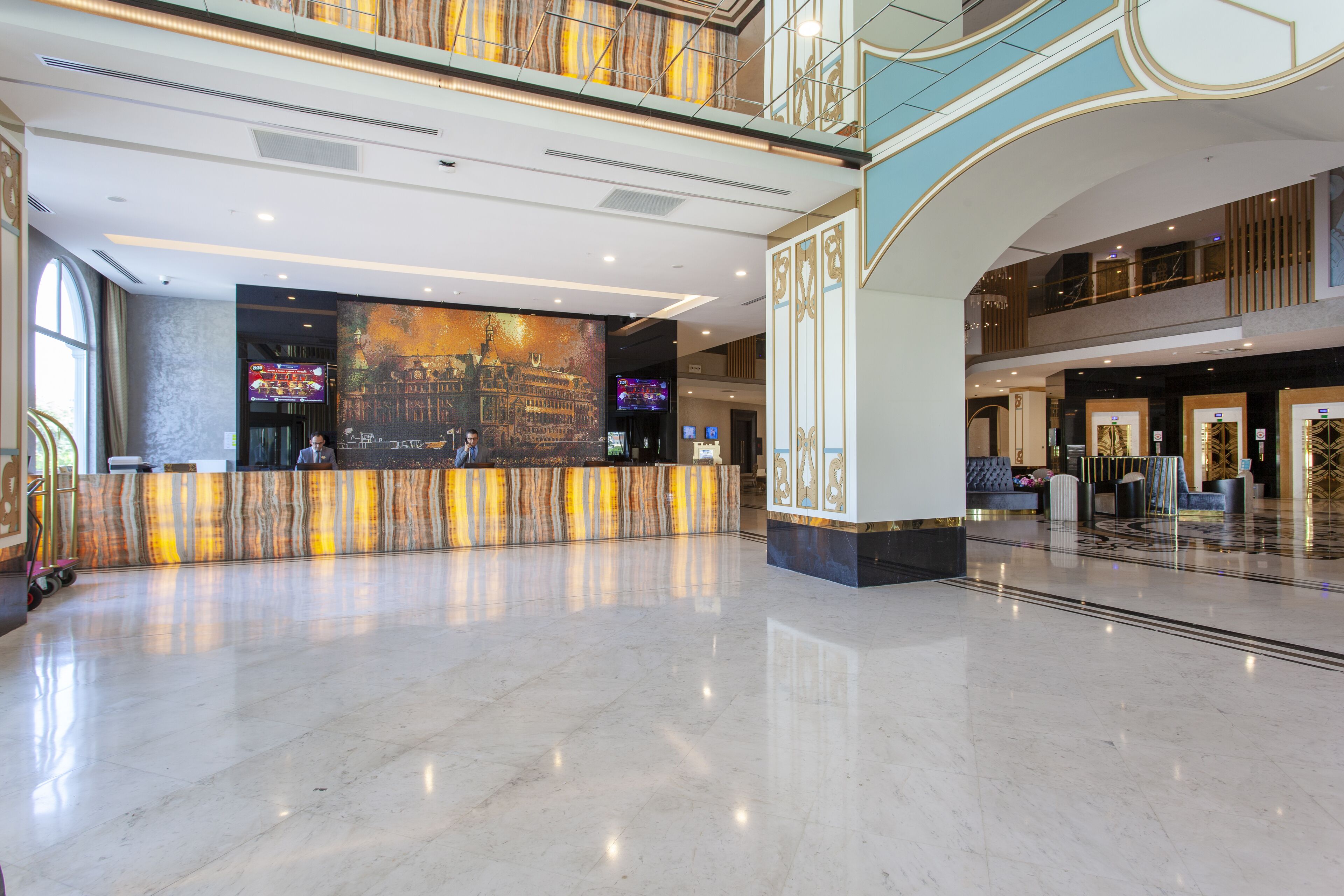 Um hall amplo com piso de mármore, balcão de recepção e uma grande tela digital exibindo uma vista urbana.