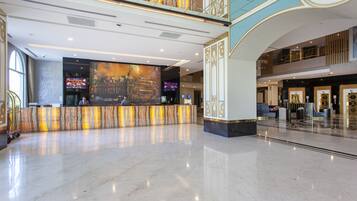 Um hall amplo com piso de mármore, balcão de recepção e uma grande tela digital exibindo uma vista urbana.