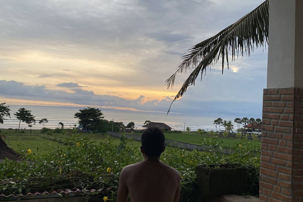Una persona sentada sobre un piso de baldosas, mirando el mar y un atardecer.