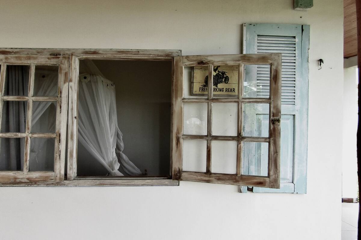 Una habitación con un ventanal grande, una ventana más pequeña con contraventanas y un cartel en la pared.