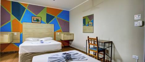 Habitación de hotel con dos camas, ventilador de techo, una silla y arte mural geométrico y colorido.