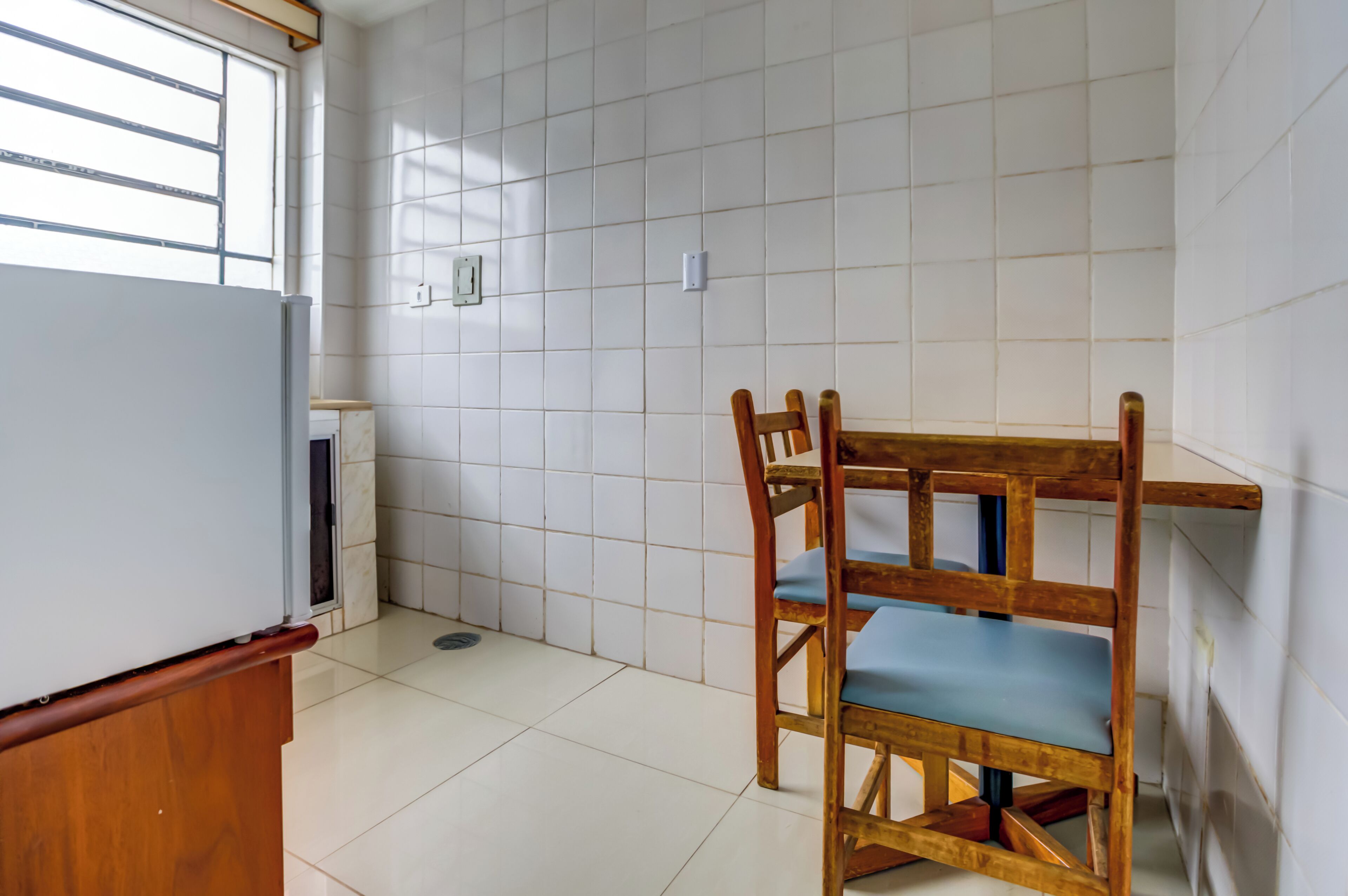 A kitchen with white tiles, a wooden table with blue cushions, and a white refrigerator.