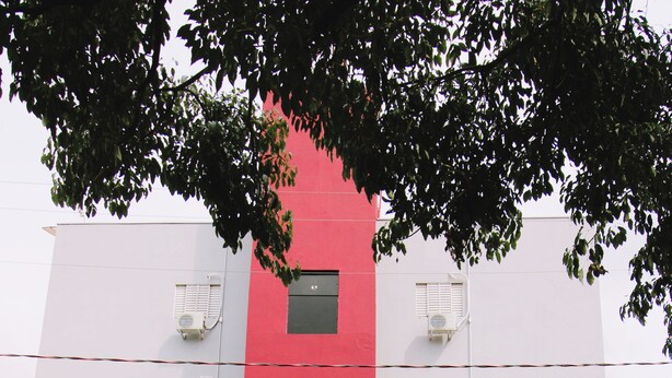 Ein mehrstöckiges Gebäude mit roter und weißer Fassade, Klimaanlagen und einem verschlossenen Eingang.