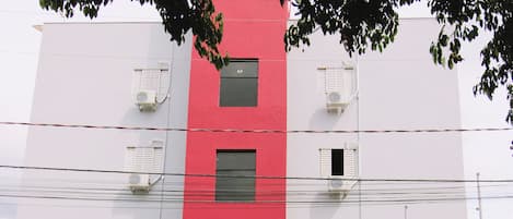 Un immeuble à plusieurs étages, doté d’une façade rouge et blanche, de climatiseurs et d’une entrée sécurisée par un portail.