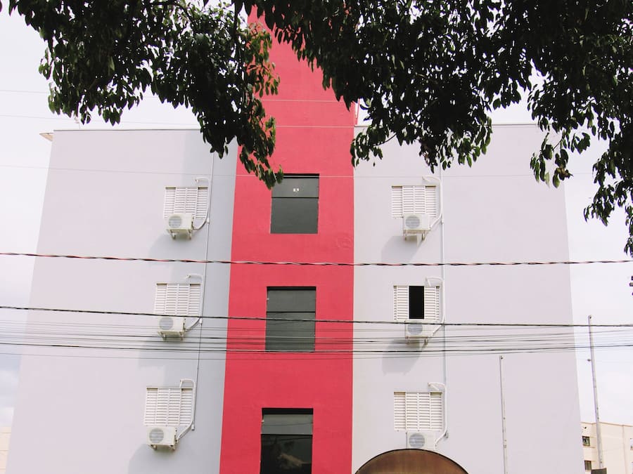 A multi-story building with a red and white facade, air conditioning units, and a gated entrance.
