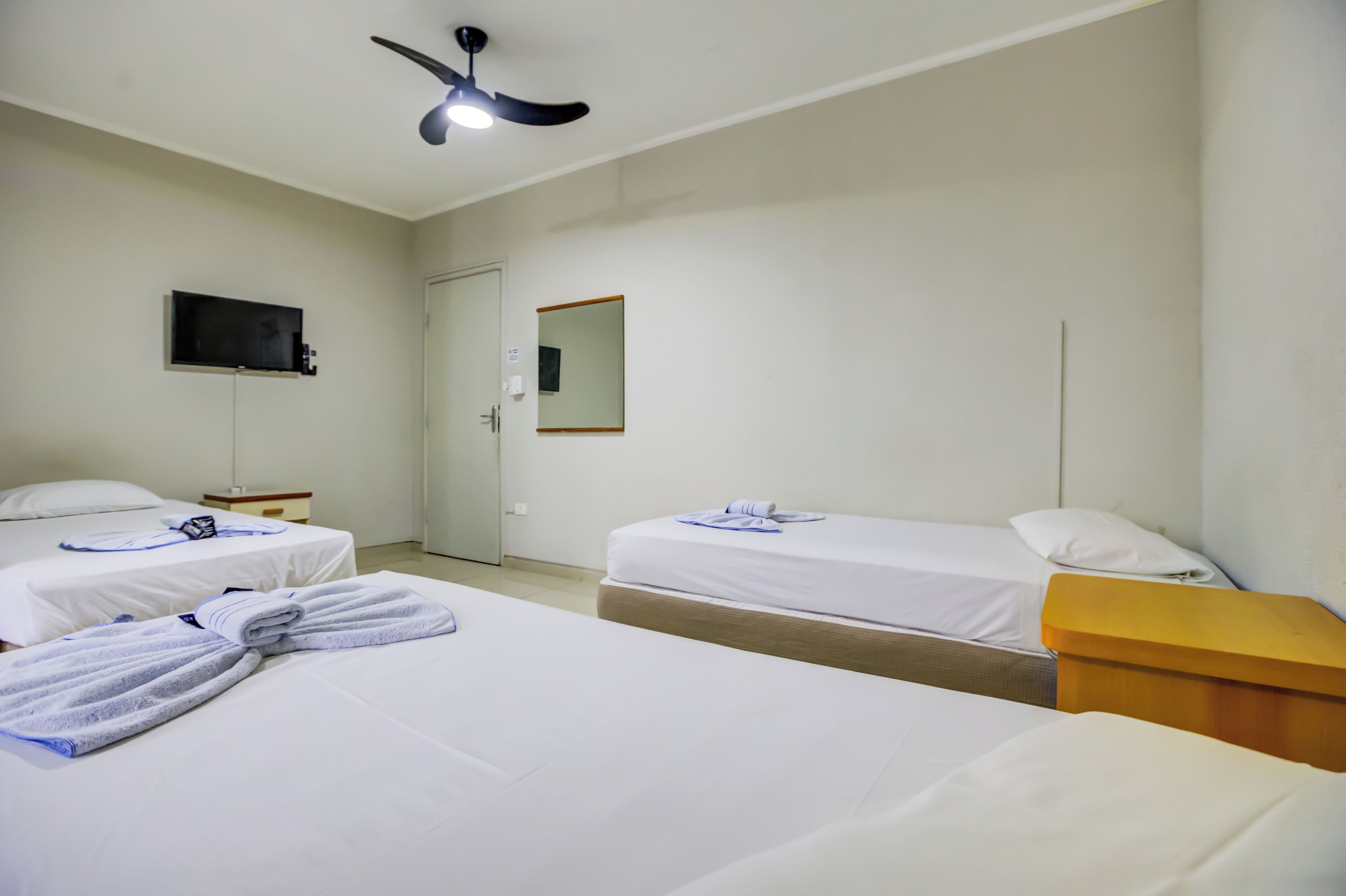 A hotel room with two beds, a flat-screen TV, a ceiling fan, and a mirror on the wall.