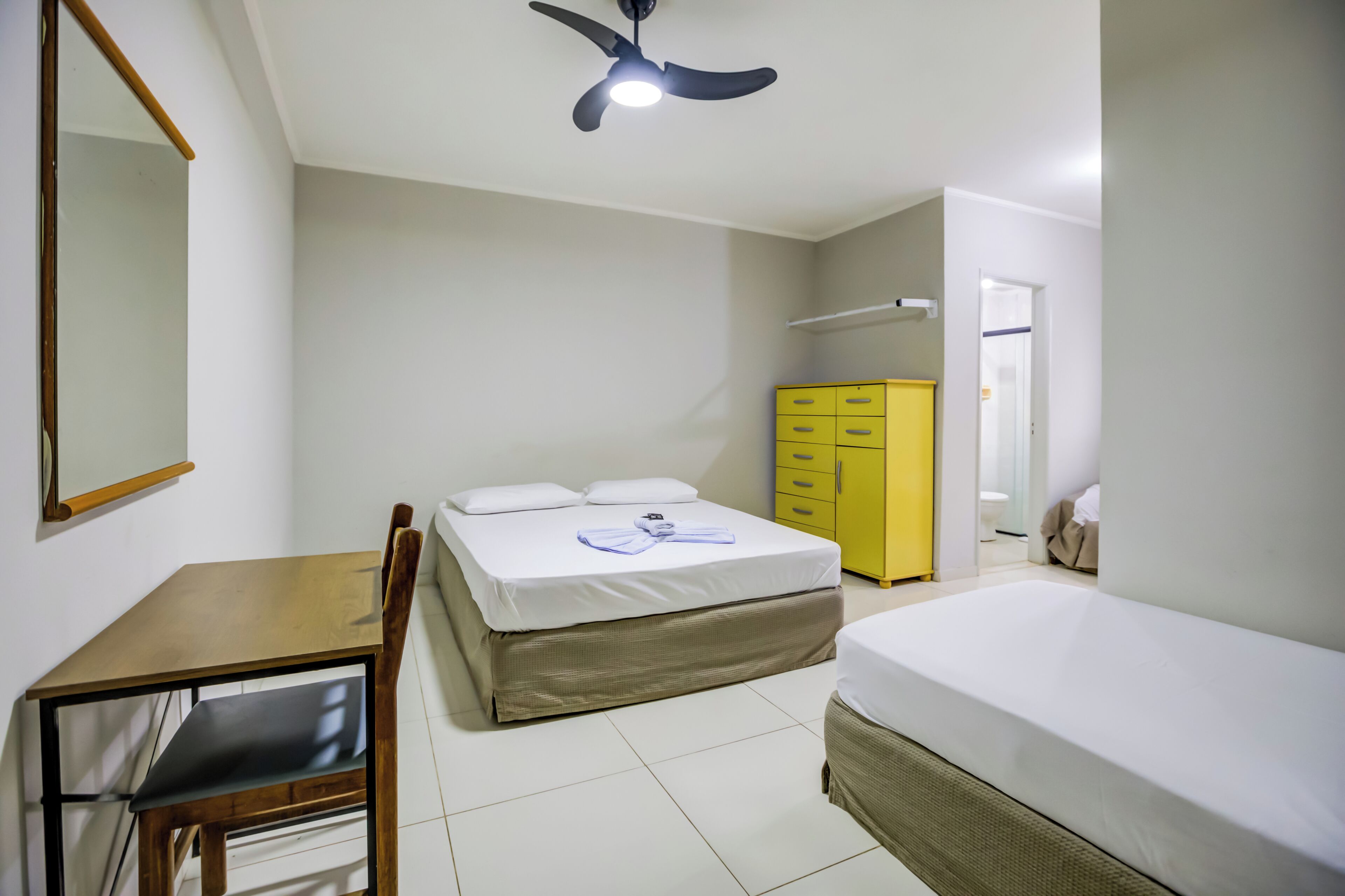 A bedroom with a bed, a desk, a chair, a wardrobe, and a ceiling fan.