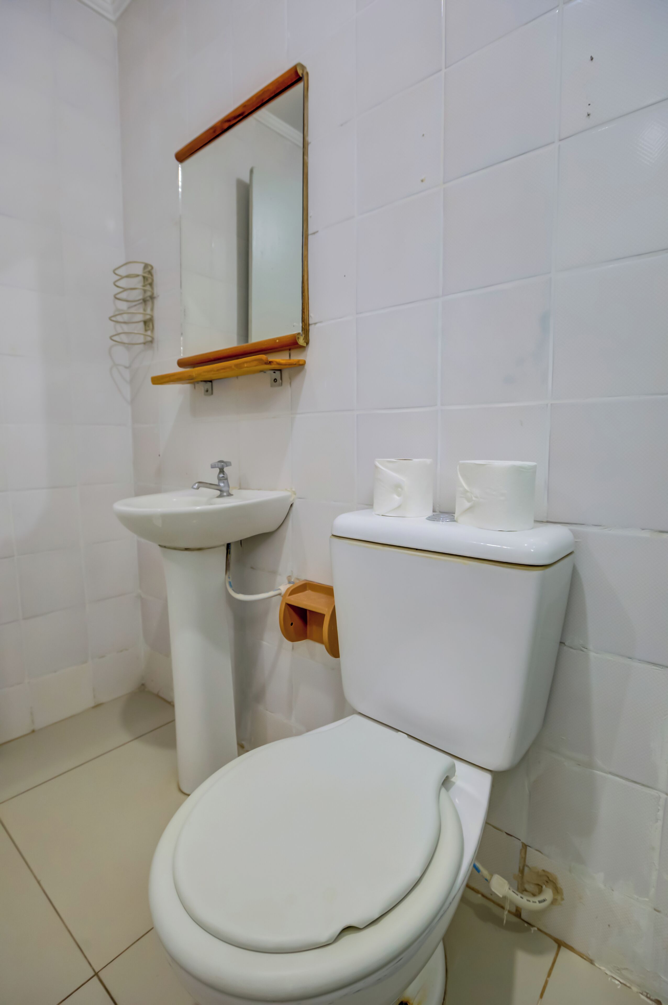A bathroom with a white toilet, a pedestal sink, and a mirror with a wooden frame.
