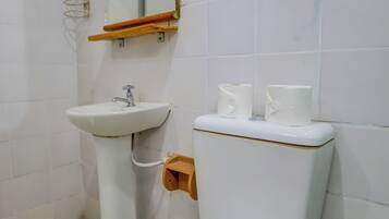Un baño con inodoro blanco, lavamanos pedestal y espejo con marco de madera.