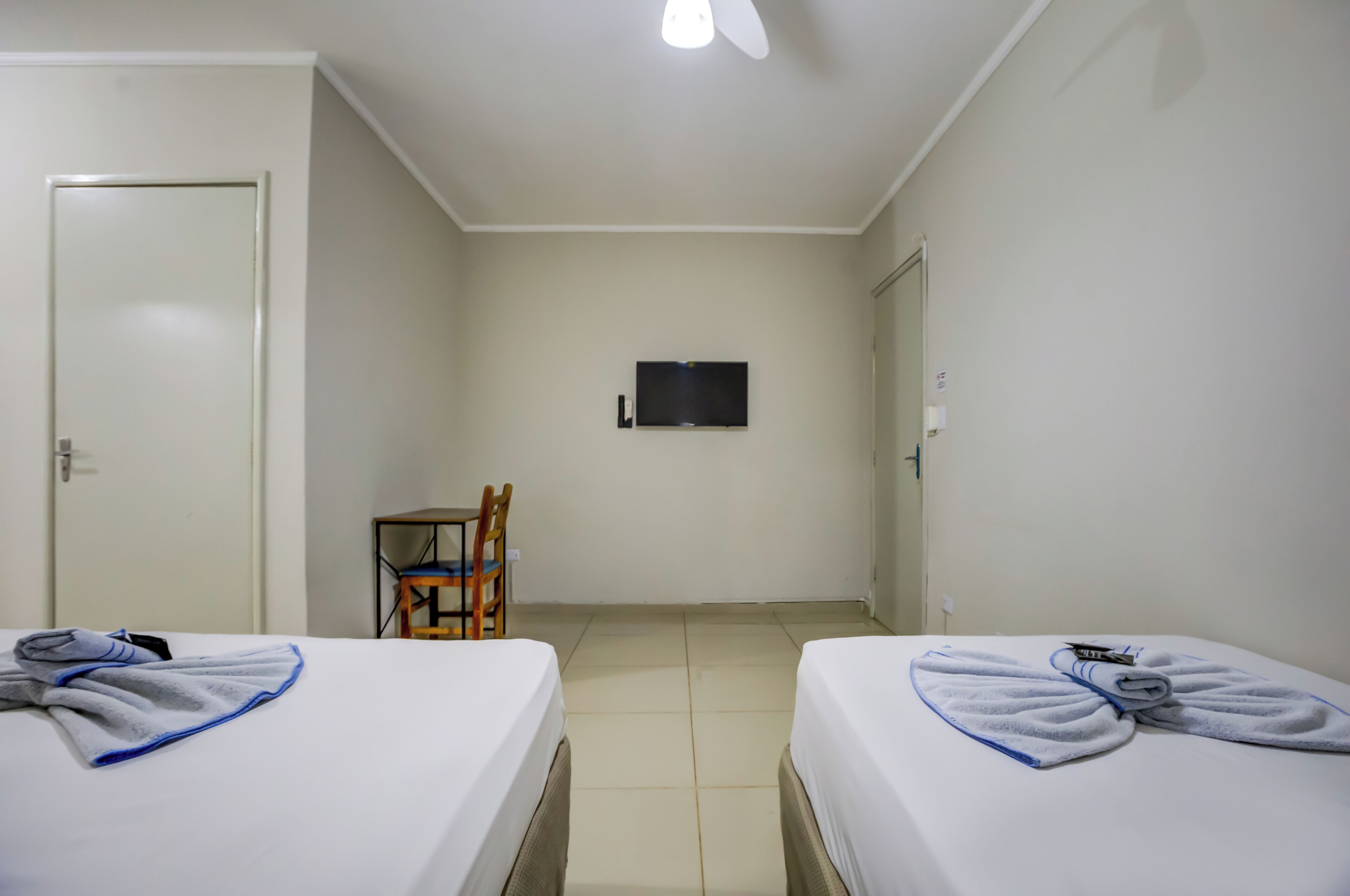 A hotel room with two beds, a chair, a television on the wall, and a door.