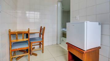 Una pequeña cocina equipada con un refrigerador blanco, una mesa de madera con sillas azules y paredes con azulejos blancos.