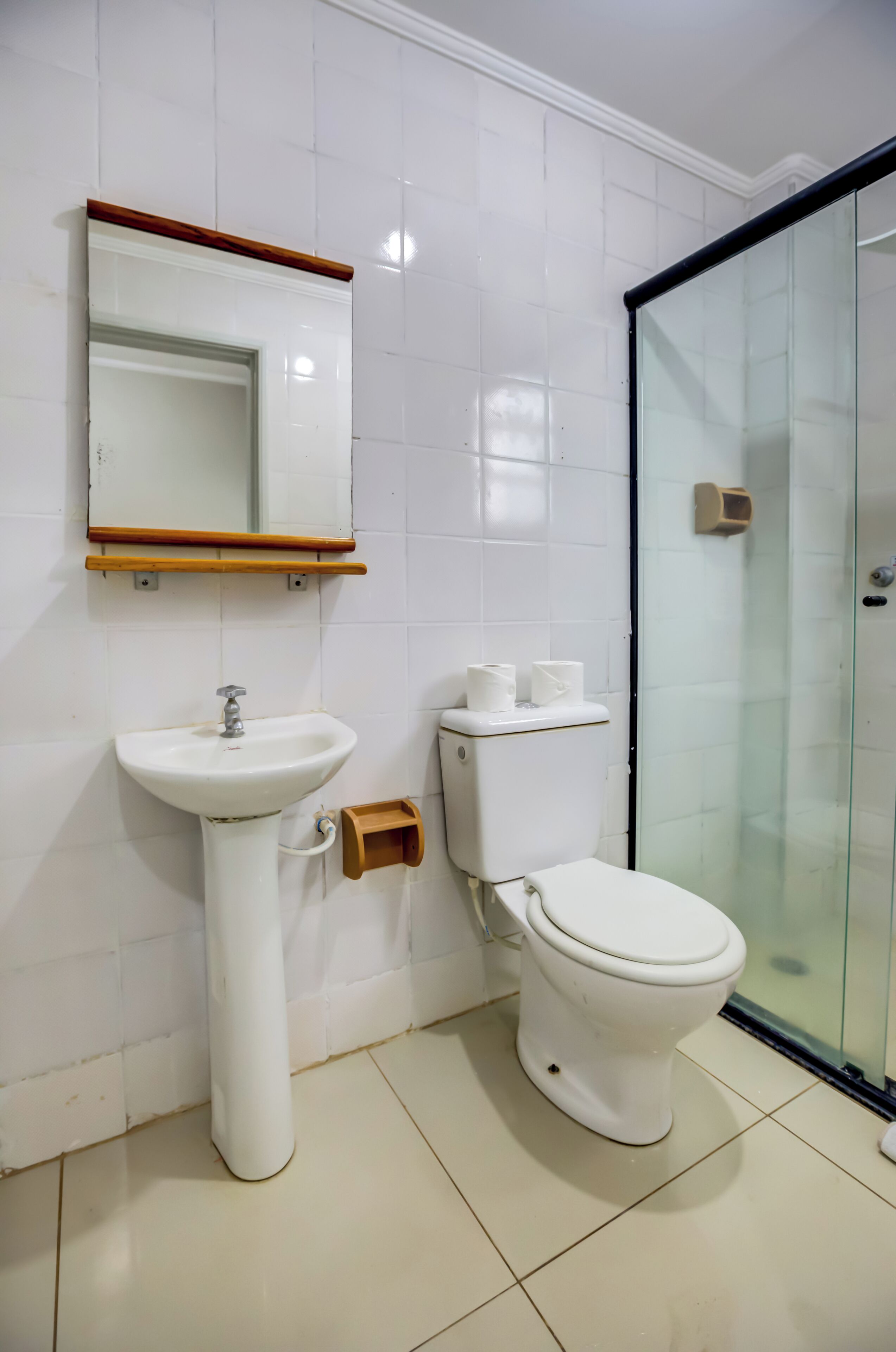 Un baño con lavabo blanco, espejo, inodoro y cabina de ducha con mampara de vidrio.