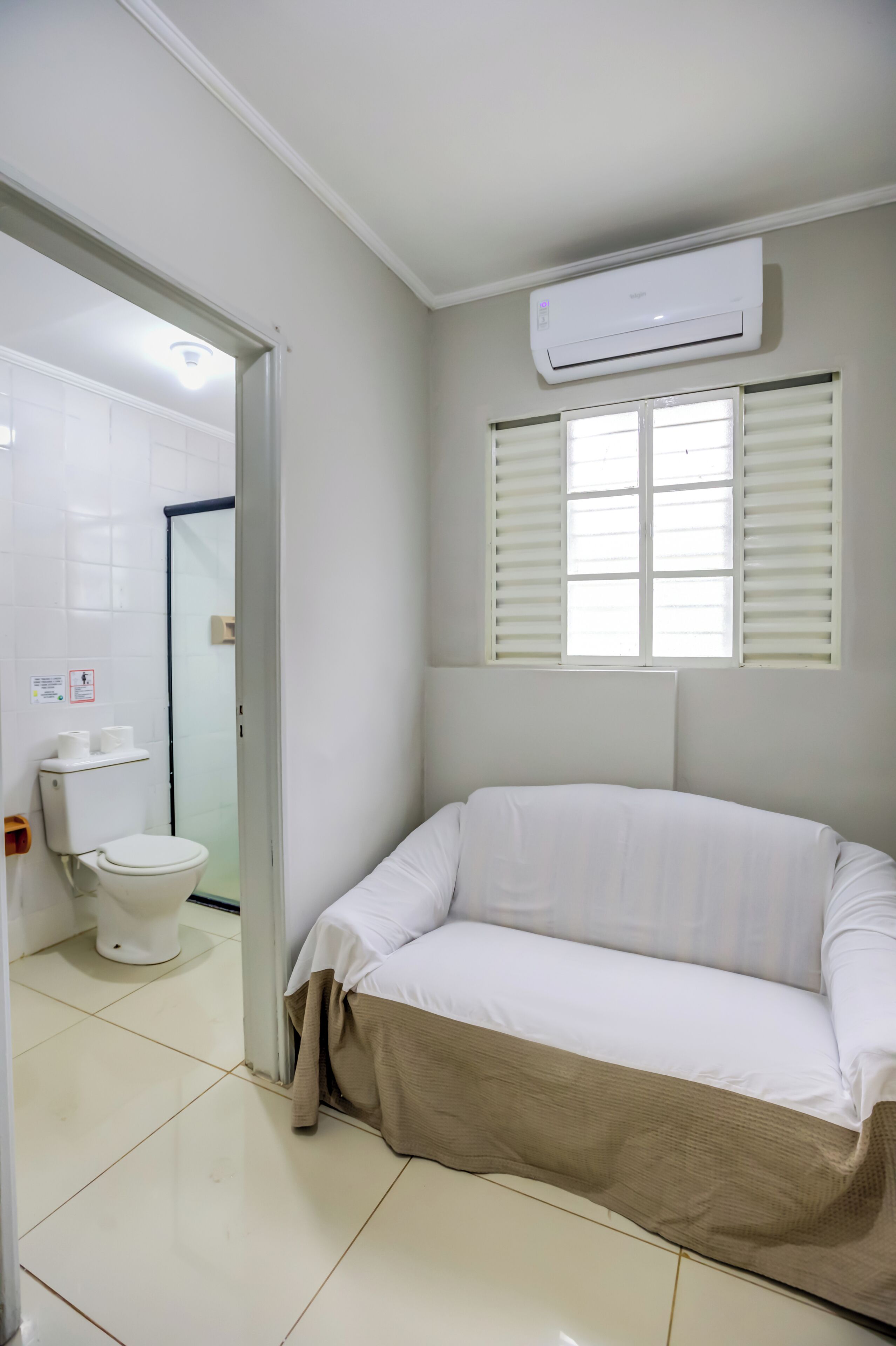 A bathroom with a toilet, a white sink, and a white air conditioner mounted on the wall.