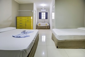 Quarto de hotel com duas camas, um guarda-roupa amarelo, uma janela com persianas e um aparelho de ar condicionado.