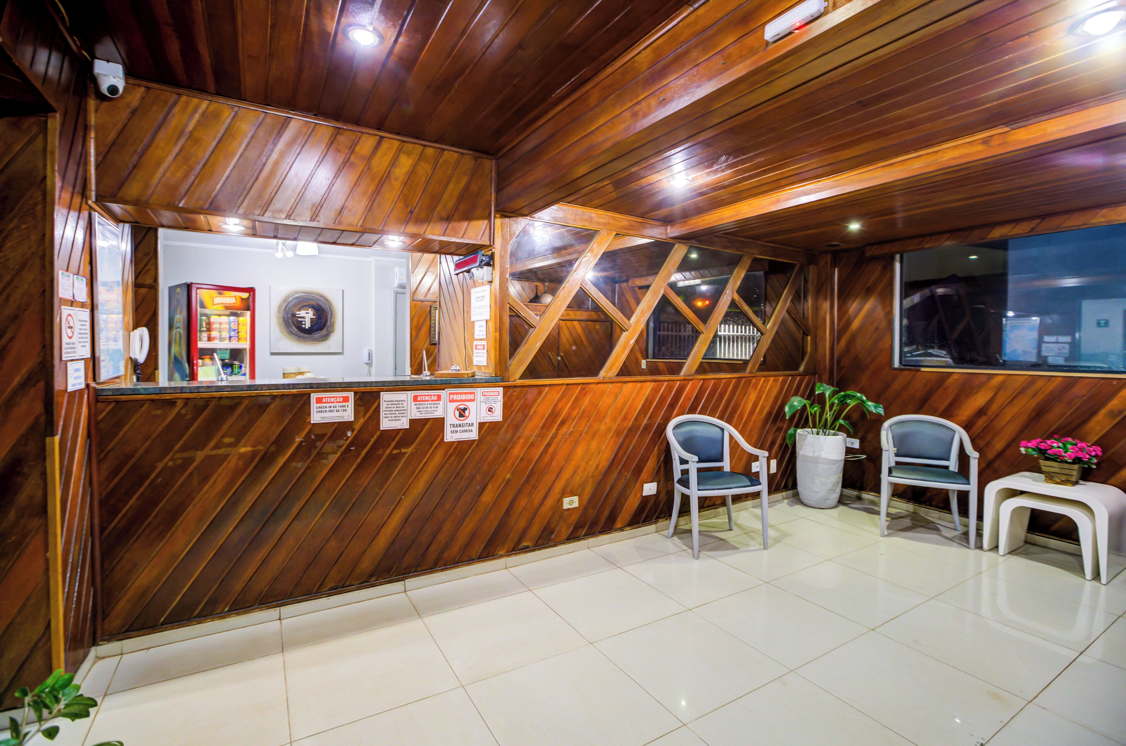 Zona de recepción con detalles de madera, mostrador de recepción, asientos e una planta en maceta.