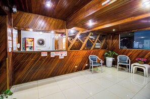 Zona de recepción con detalles de madera, mostrador de recepción, asientos e una planta en maceta.