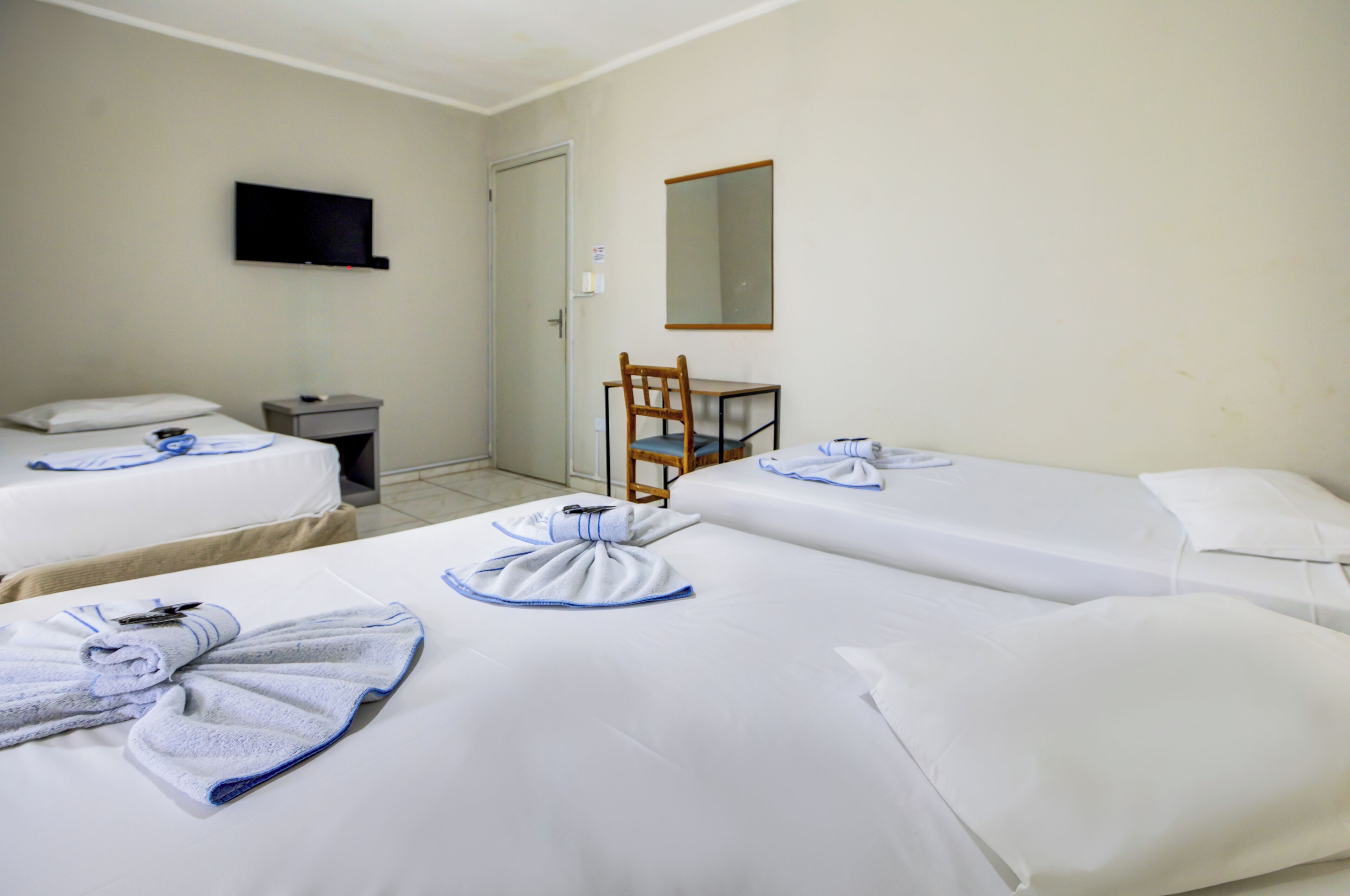 Ein Hotelzimmer mit zwei Betten, einem Sessel, einem Schreibtisch, einem Fernseher und einer Tür.