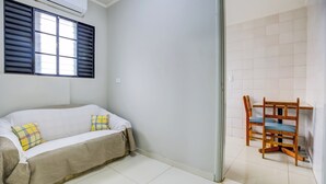 Une pièce avec un canapé, un fauteuil et une fenêtre équipée de stores.