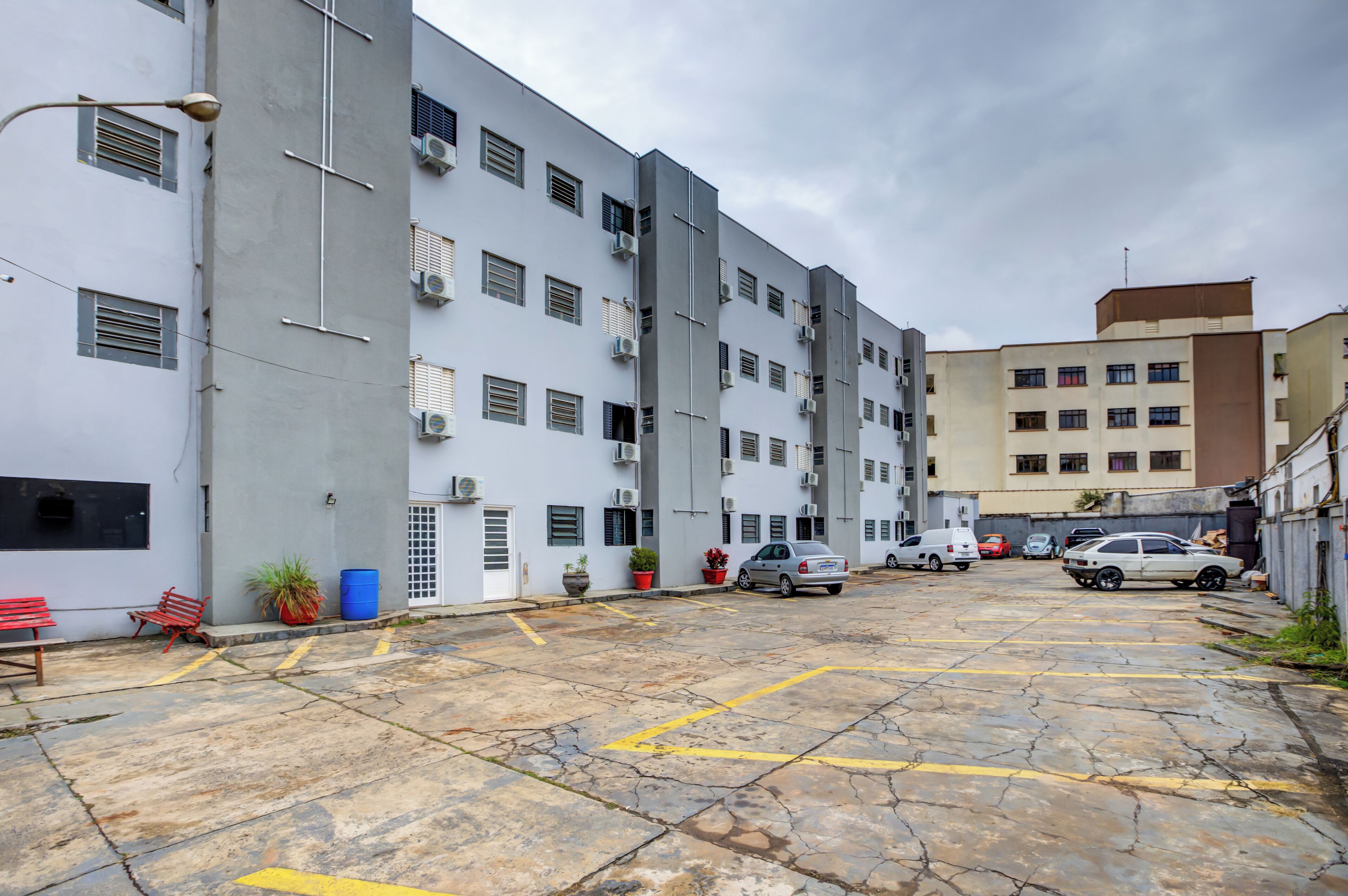 A parking area with multiple cars, a building with air conditioning units, and a few potted plants.