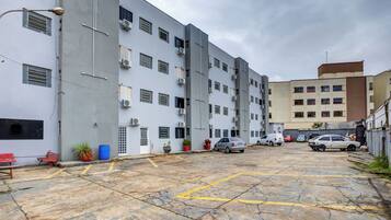 A parking area with multiple cars, a building with air conditioning units, and a few potted plants.