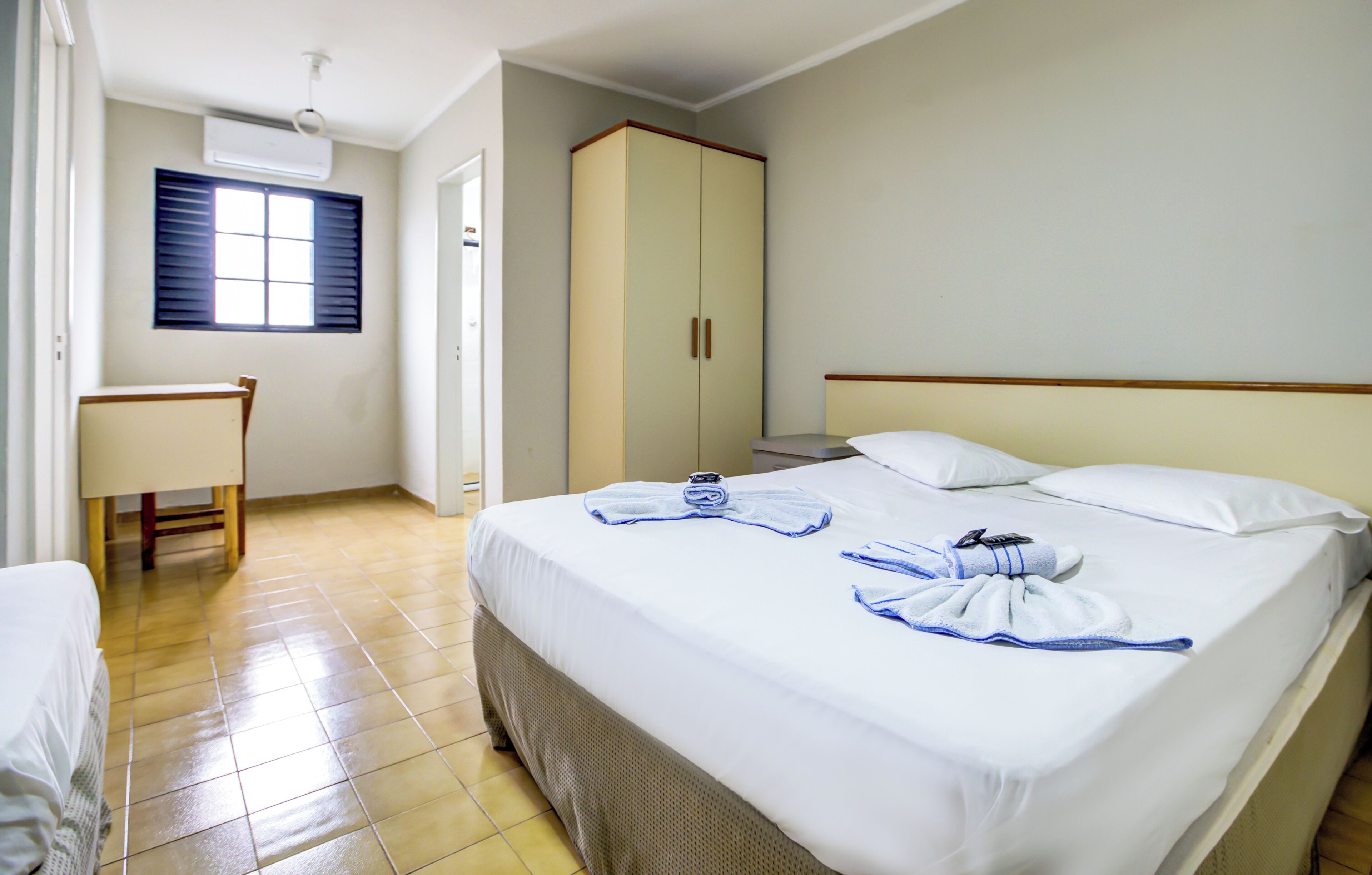 Una habitación de hotel con cama, escritorio, armario y ventana.
