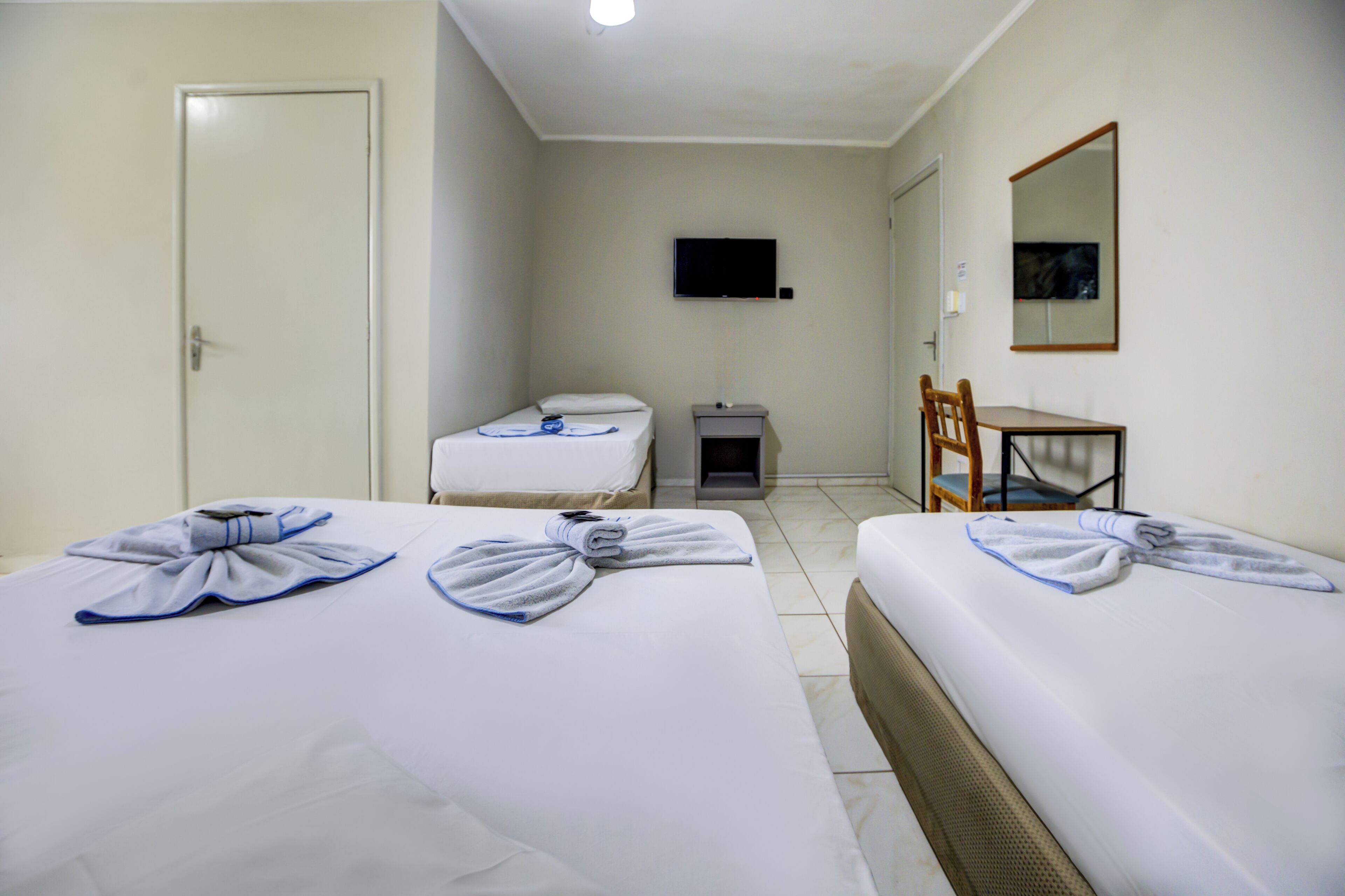 A hotel room with two beds, a desk, a chair, a television, and a mirror.