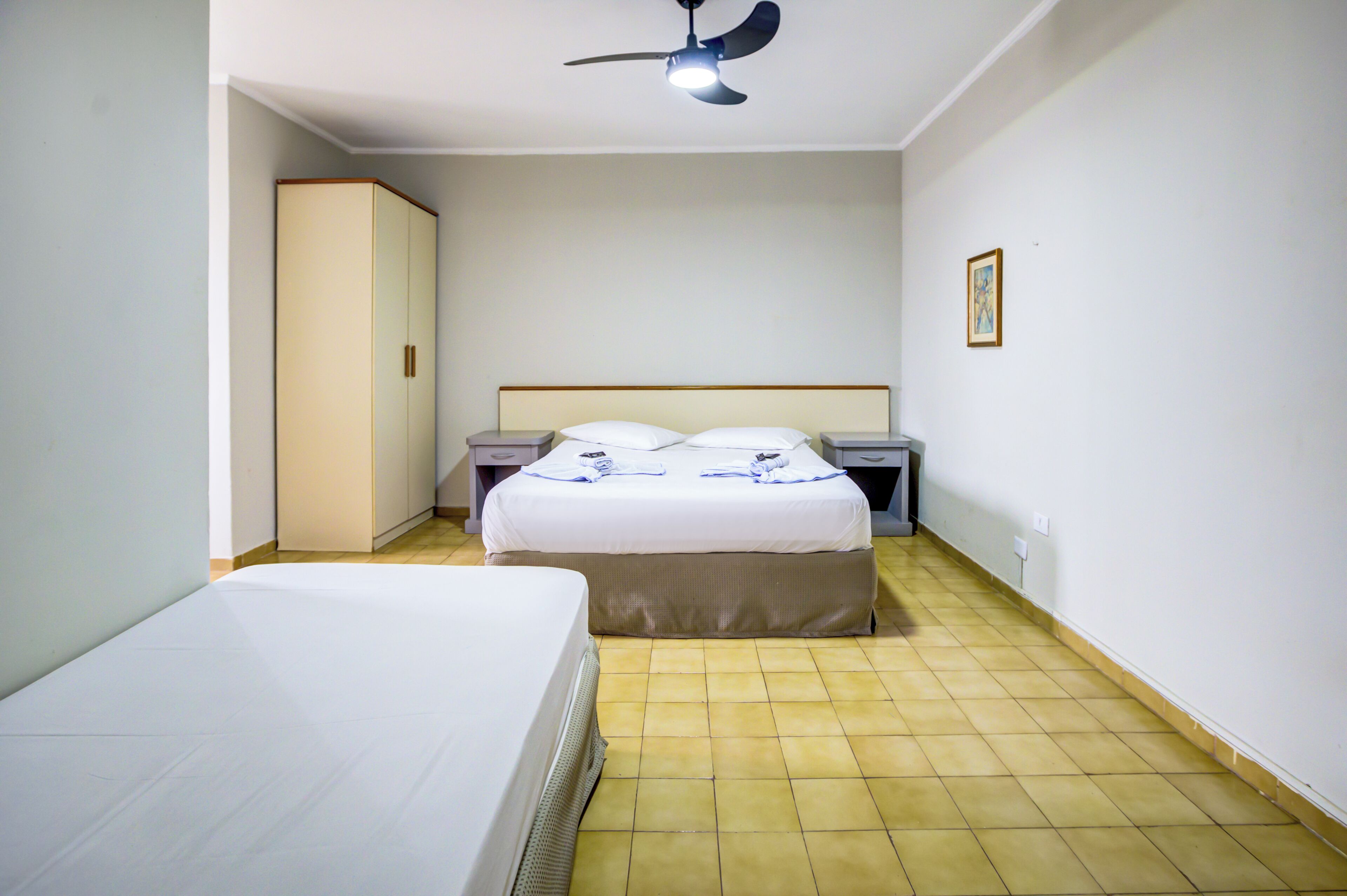 Habitación de hotel con una cama individual, una mesita de noche, un armario y un ventilador de techo.