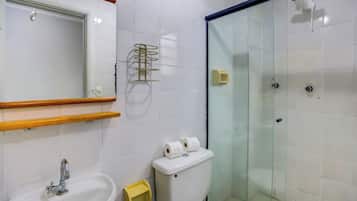 Casa de banho com lavatório, sanita e cabine de chuveiro com parede de vidro.